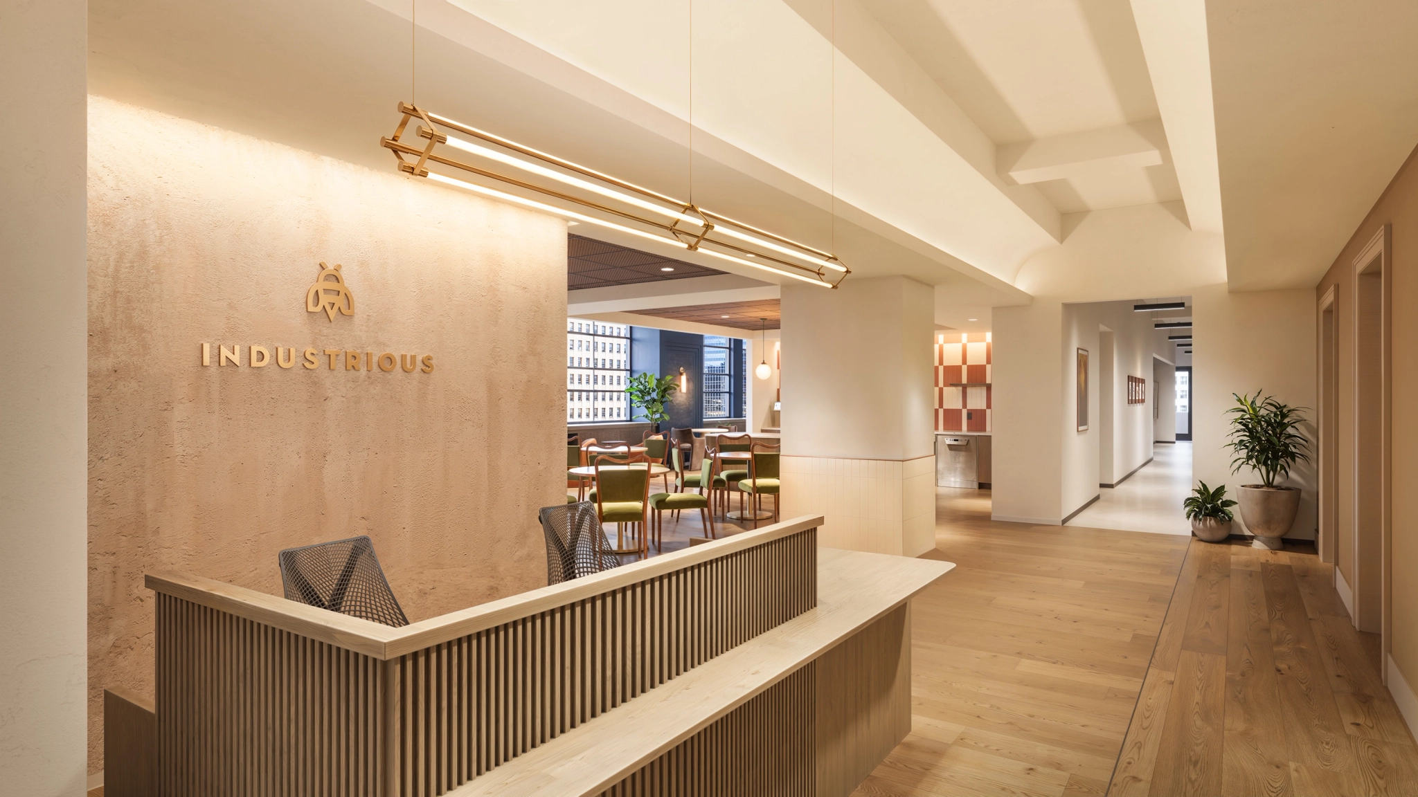 Reception area of a coworking office space featuring a wooden desk, “Industrious” logo on the wall, modern decor with plants, seating area in the background, and abundant natural light.