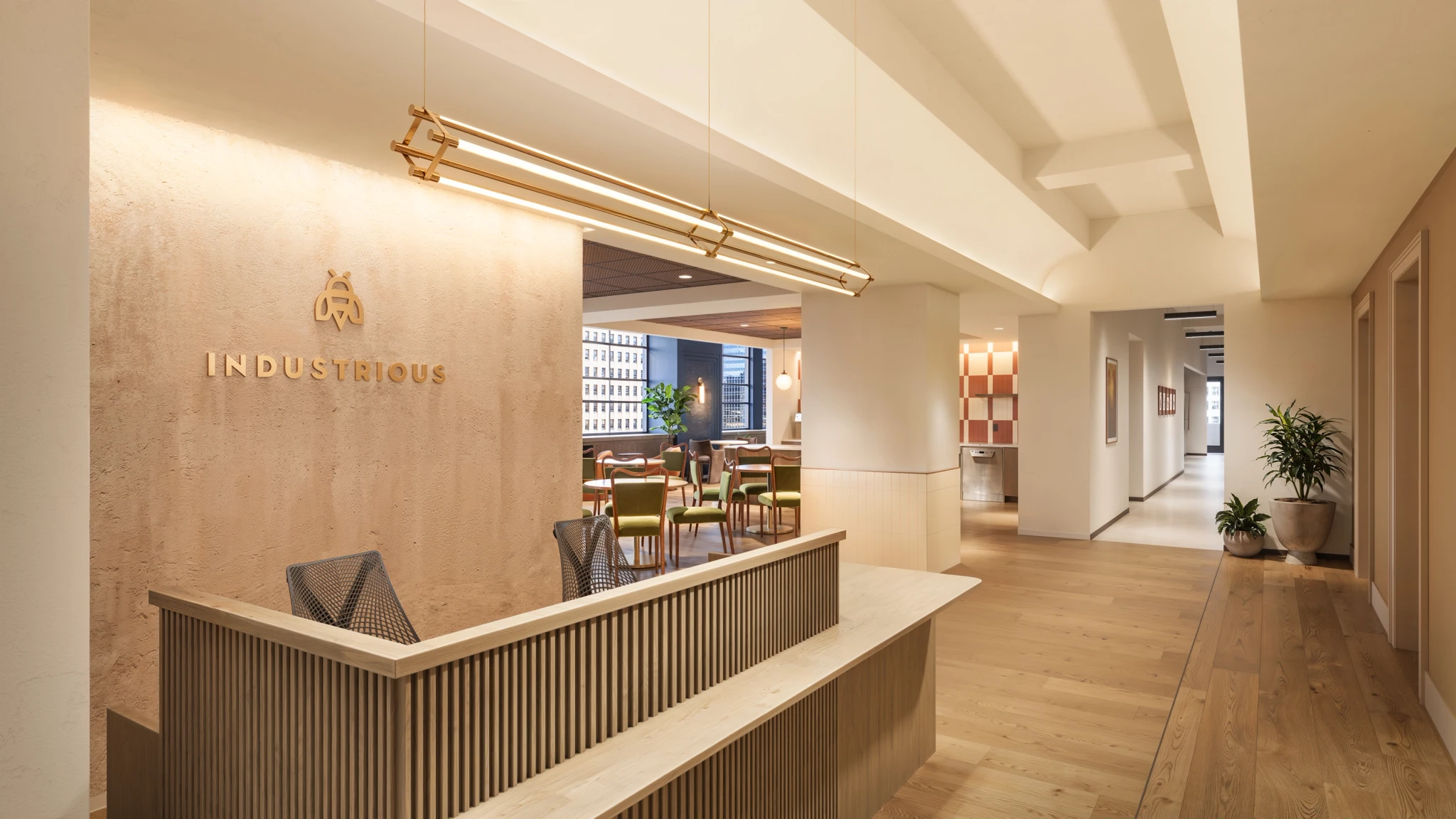 Reception area of a coworking office space featuring a wooden desk, “Industrious” logo on the wall, modern decor with plants, seating area in the background, and abundant natural light.