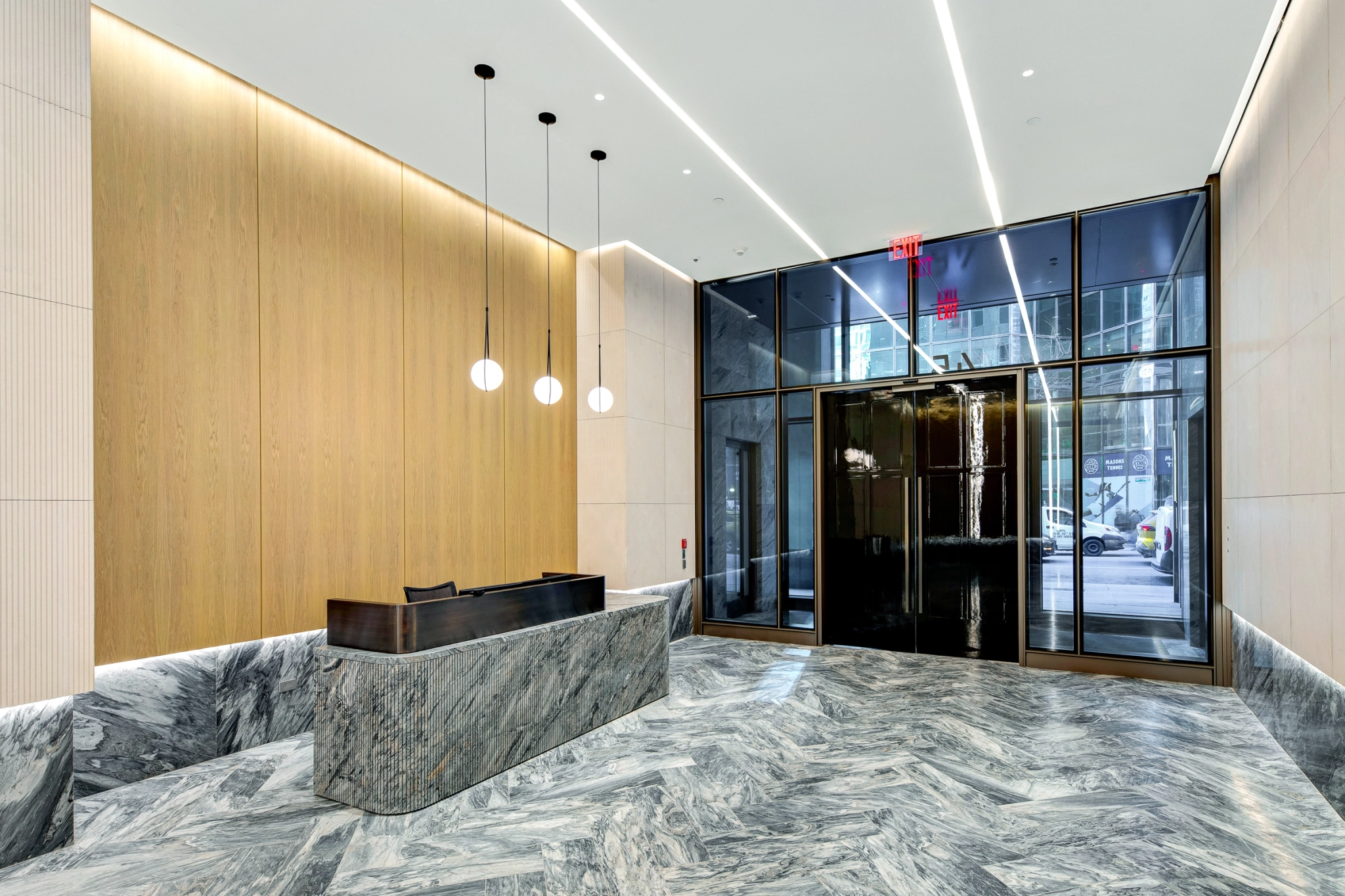Modern coworking office lobby with a marble reception desk, wood-paneled wall, three hanging lights, and glass entrance doors facing a bustling New York city street.