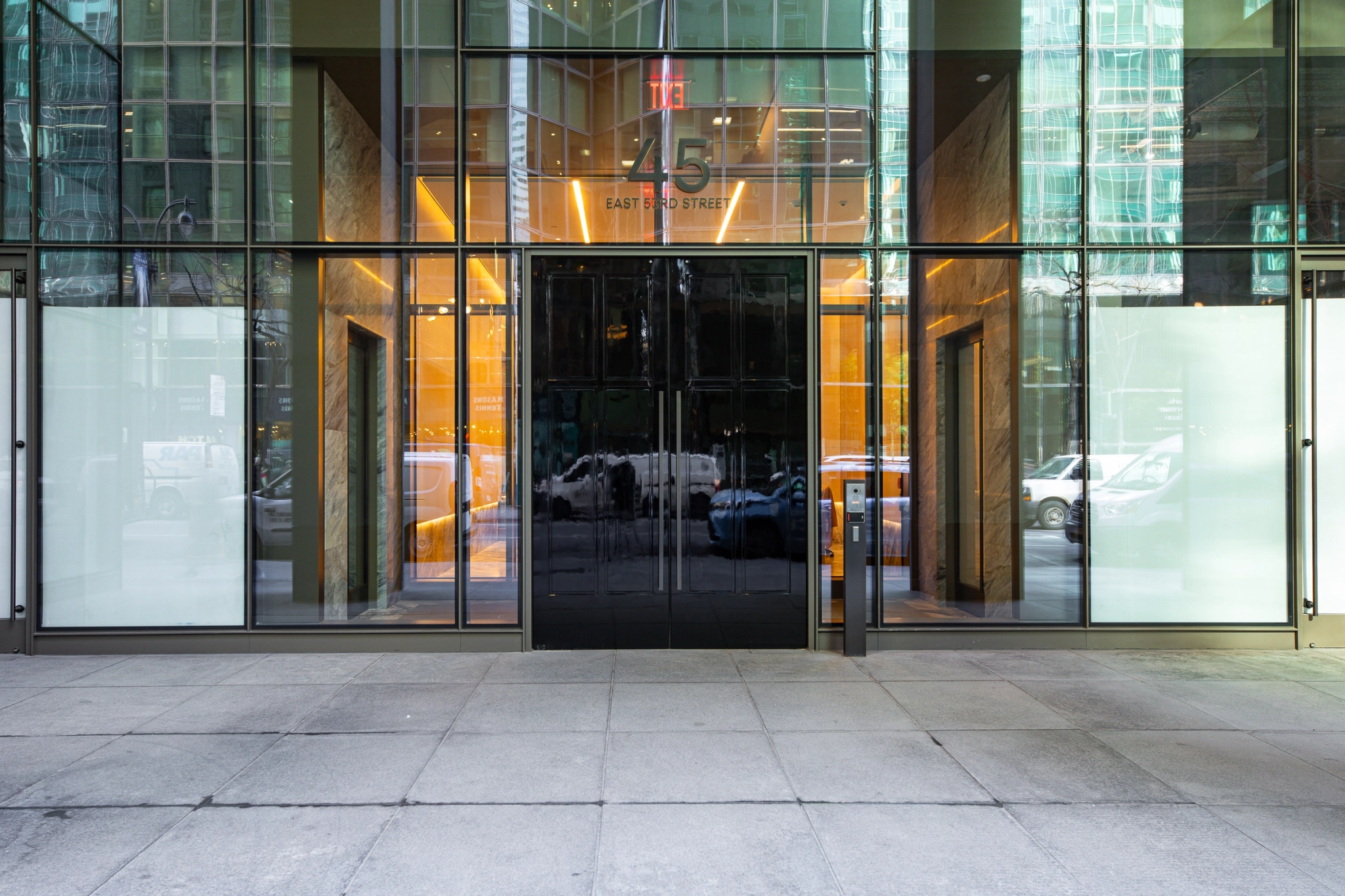 Glass entrance of a modern New York office building at "45 East 53rd Street," reflecting cars and surrounding buildings—an inviting spot for coworking professionals.