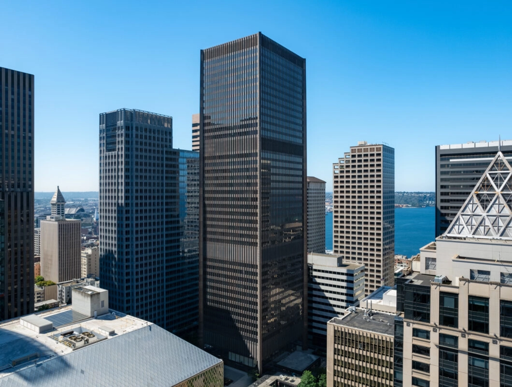 View of the Seattle city skyline with several tall office buildings, including a prominent dark skyscraper in the center, under a clear blue sky and water visible in the background—an inspiring workspace for productivity.