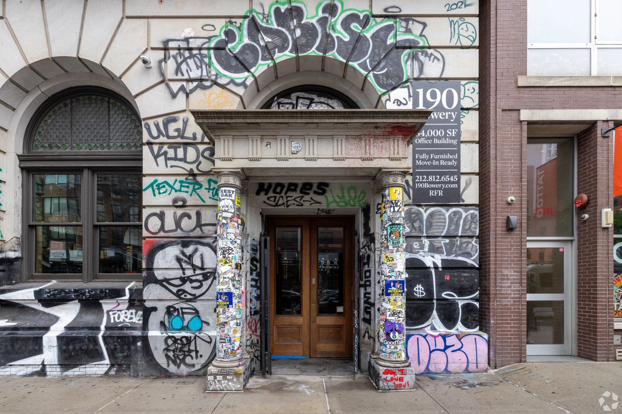 Building entrance with ornate columns and wooden doors, surrounded by extensive graffiti and stickers—evoking an edgy New York vibe outside what could be a creative office or meeting room.