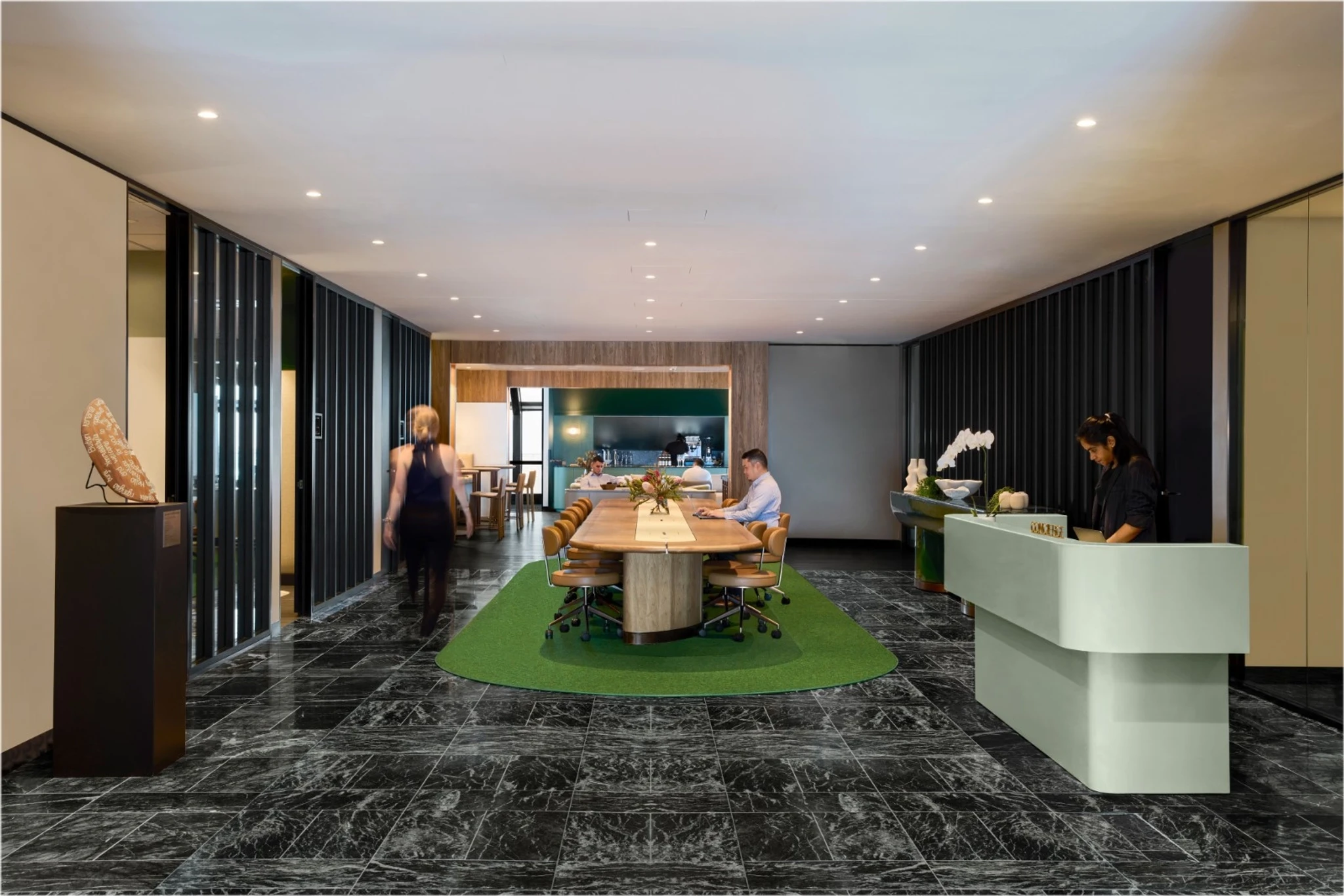 Modern office lobby in Sydney with marble flooring, a reception desk on the right, people at a central meeting table, and another person walking towards a conference area and meeting room in the background.