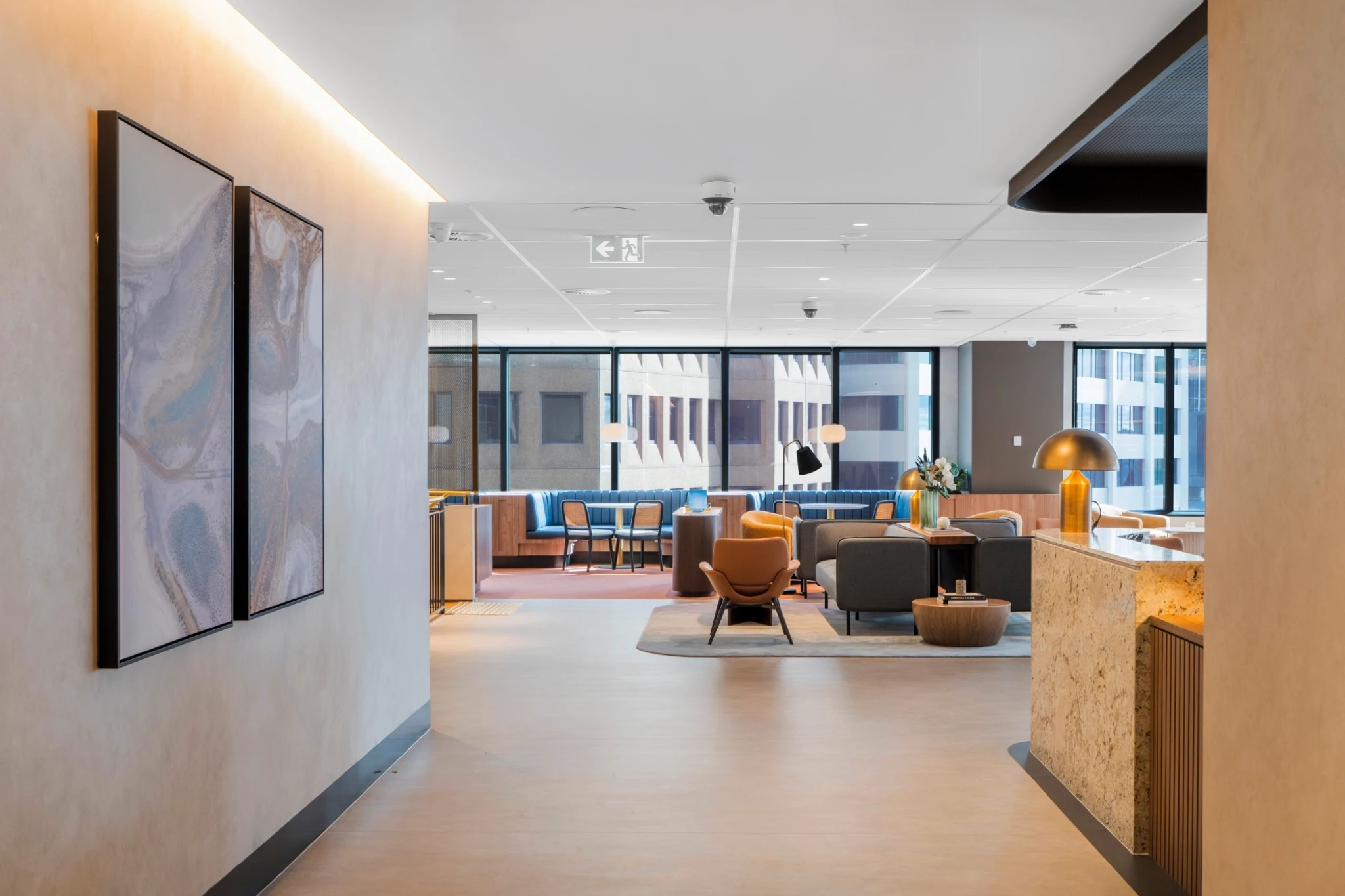 Modern Sydney office lounge with contemporary furniture, large windows, abstract wall art, and a reception desk with a gold lamp in a well-lit, open workspace.