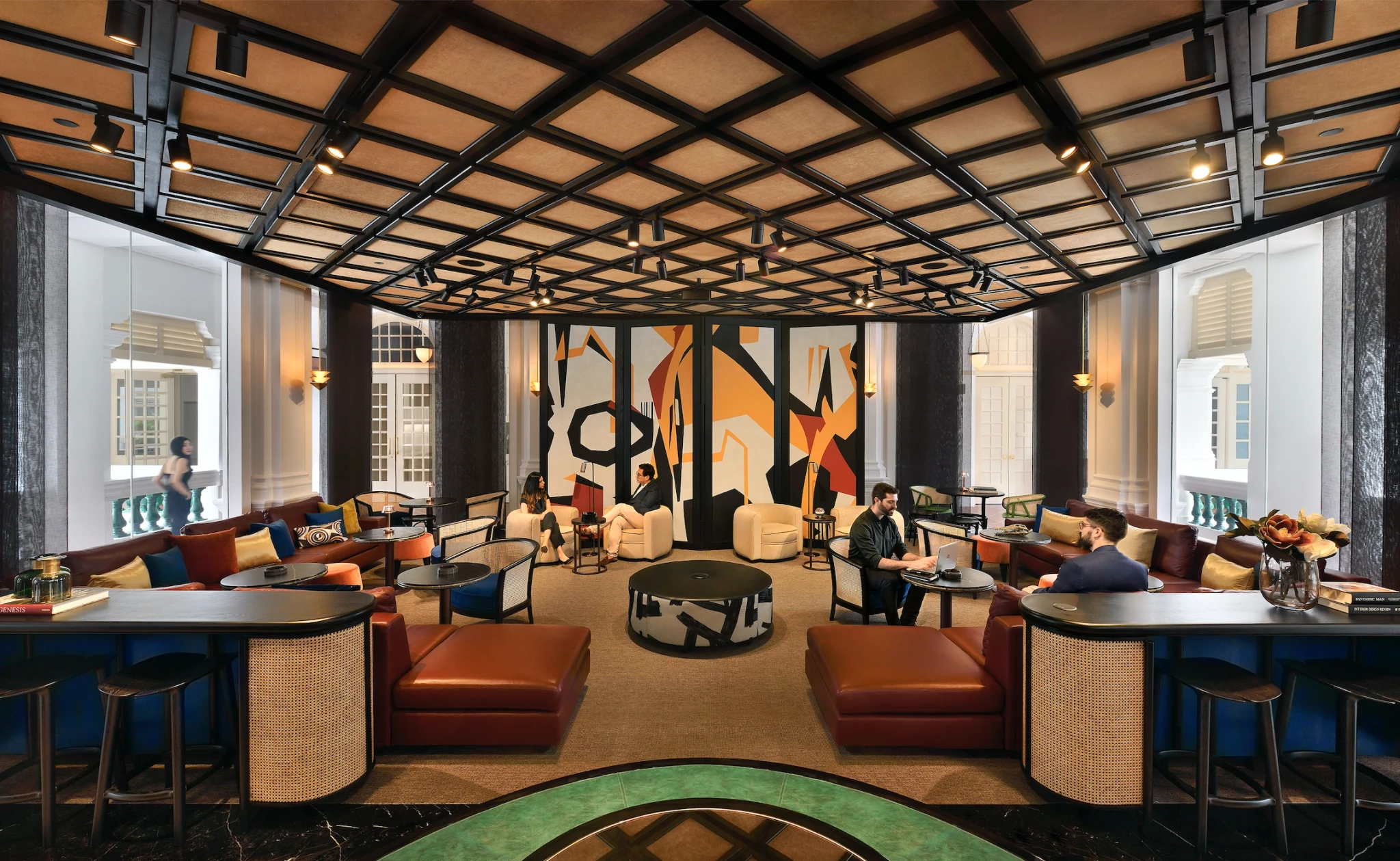 Spacious modern lounge with leather seating, round tables, abstract wall art, large windows, and people conversing and working in a vibrant coworking workspace.