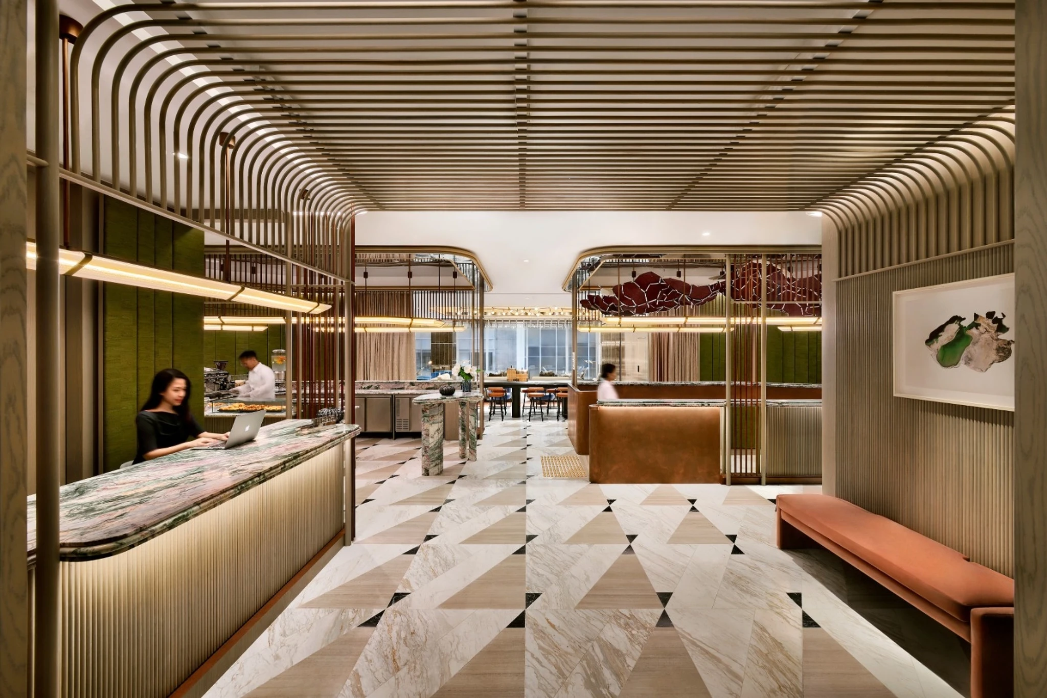 Modern hotel lobby with geometric tile flooring, marble reception desk, wooden ceiling details, bench seating, and staff attending to guests—ideal for relaxing or transitioning to the onsite meeting room and coworking workspace.