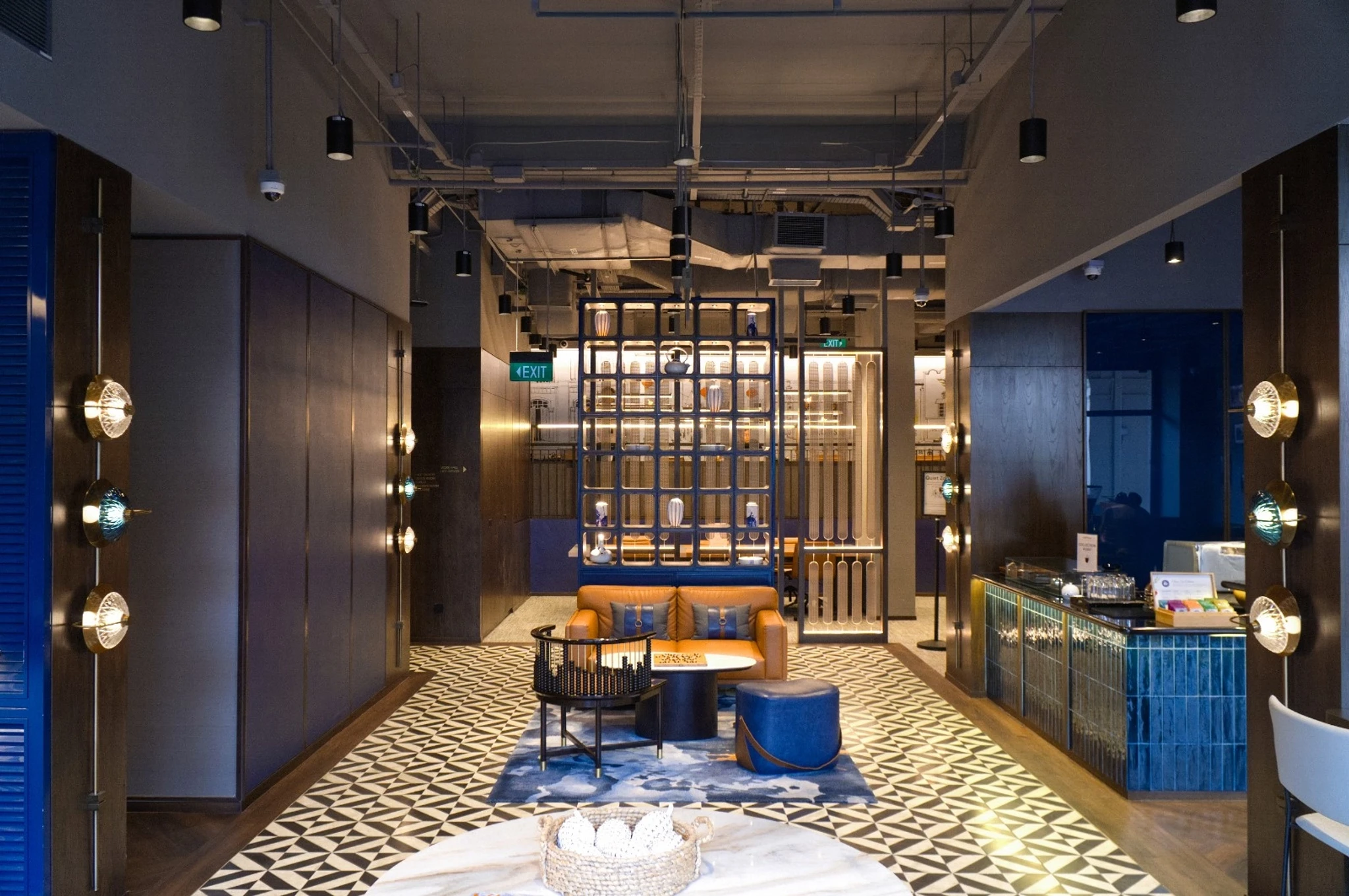 Modern lounge area with patterned flooring, blue and brown furniture, decorative lighting, and an open shelving divider creates a stylish office meeting room in a contemporary Singapore interior space.