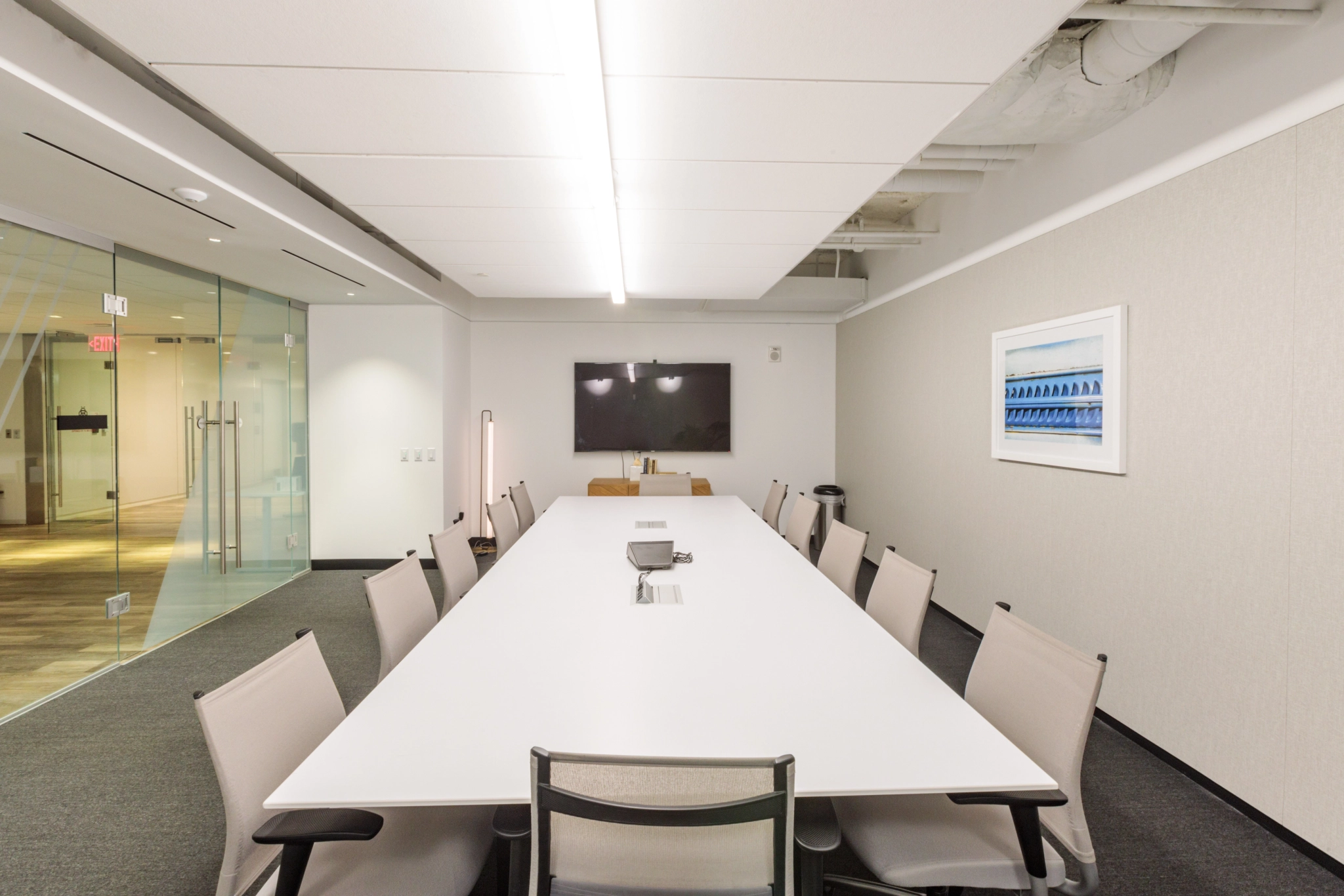 Salle de conférence moderne à Arlington avec une longue table blanche entourée de huit chaises, face à un téléviseur fixé au mur. L'espace de travail comprend un mur en verre, des œuvres d'art encadrées et un éclairage au plafond.