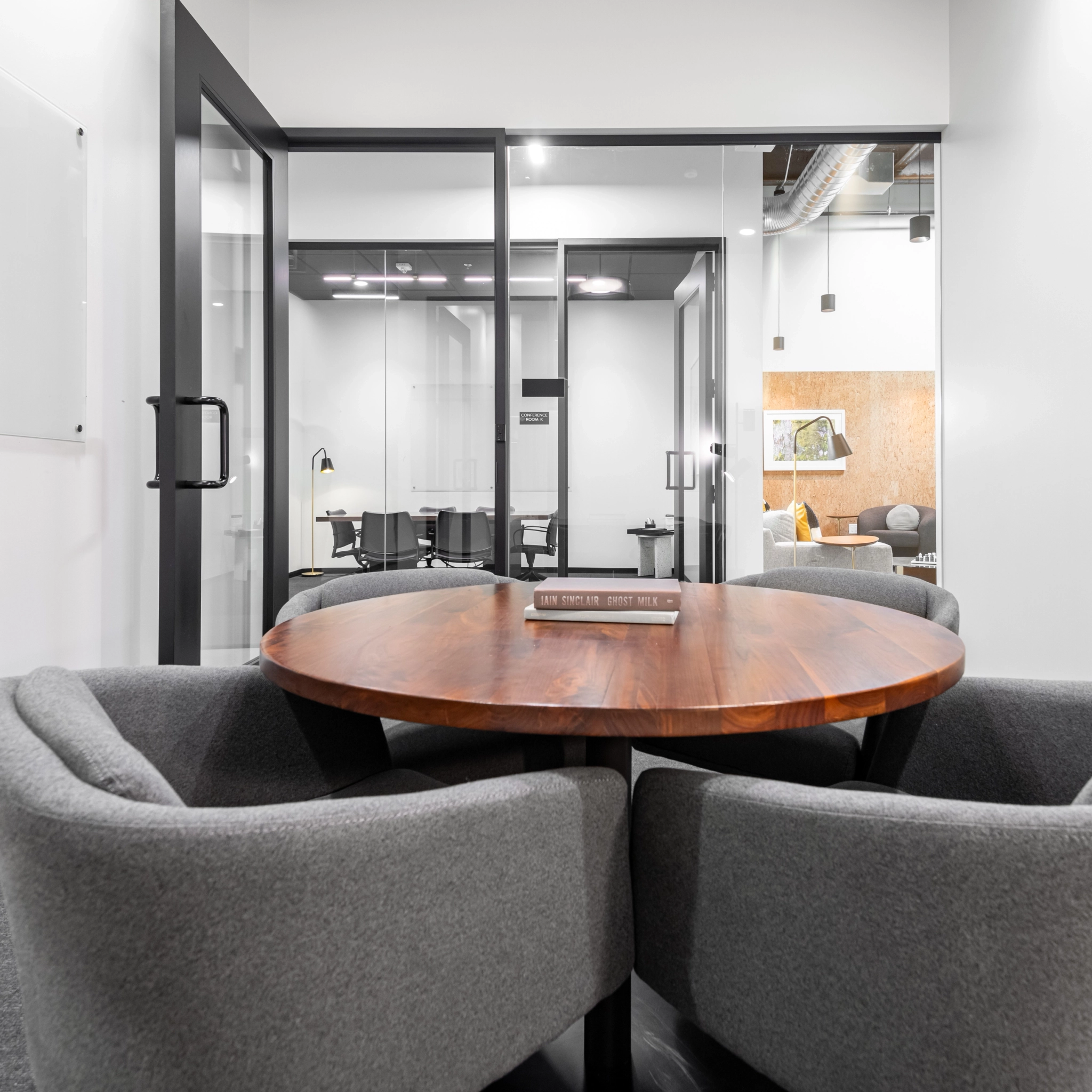 A Walnut Creek workspace featuring a round wooden table and four gray chairs, perfectly positioned in front of the sleek glass office doors.