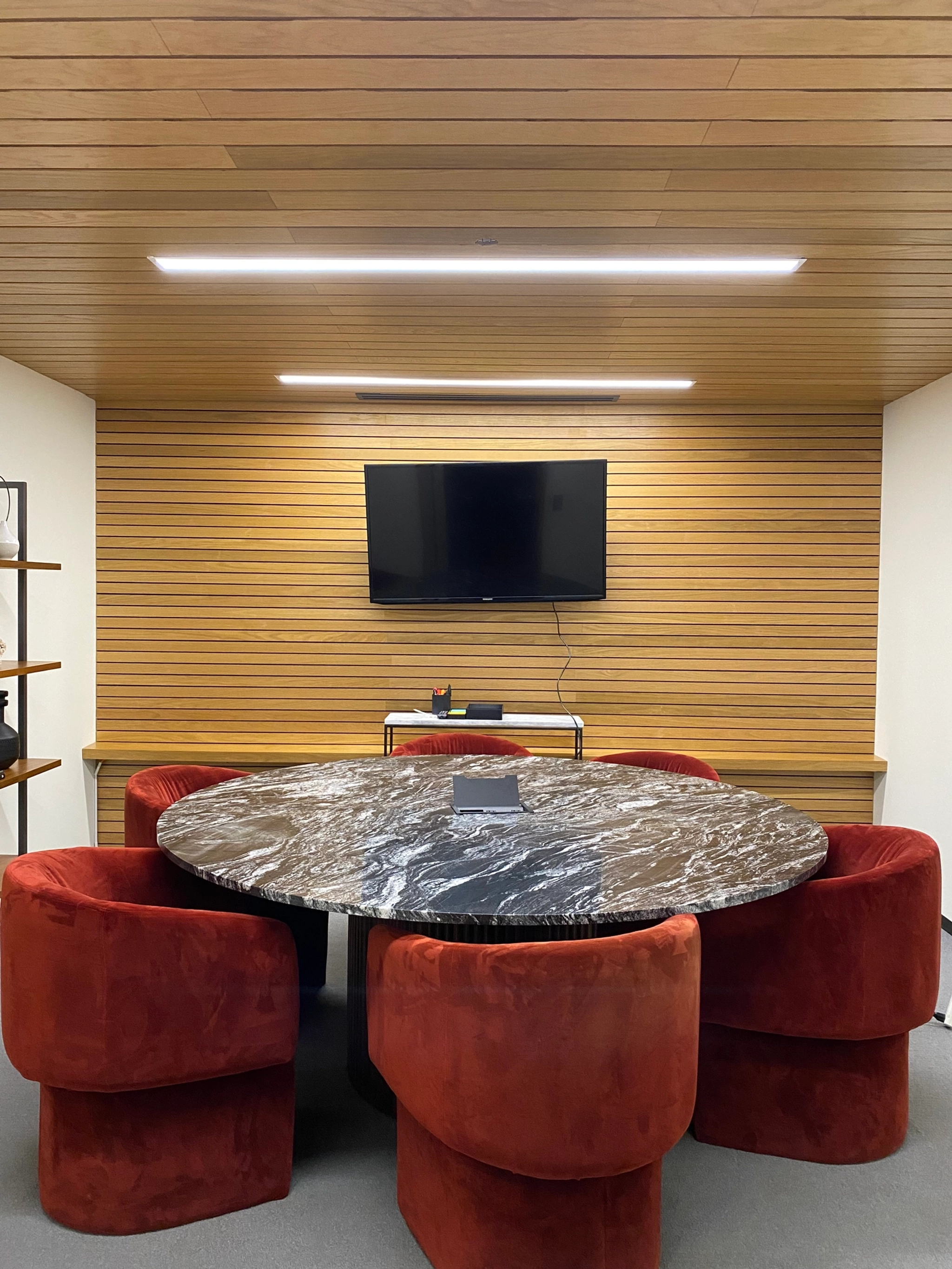 A meeting room in Atlanta features a round marble table, red velvet chairs, a wall-mounted TV, and elegant wooden paneling, creating the perfect workspace for collaboration.