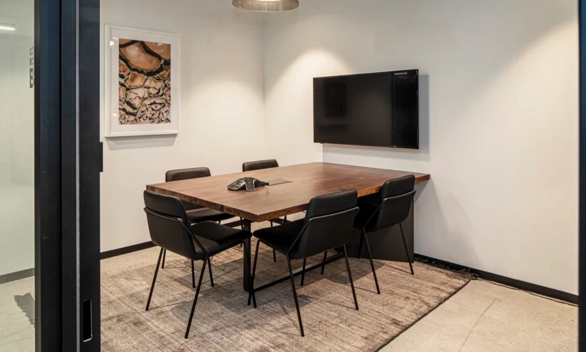 Salle de conférence de bureau moderne à Atlanta avec une table en bois, six chaises noires, une télévision au mur et une œuvre d'art abstrait.