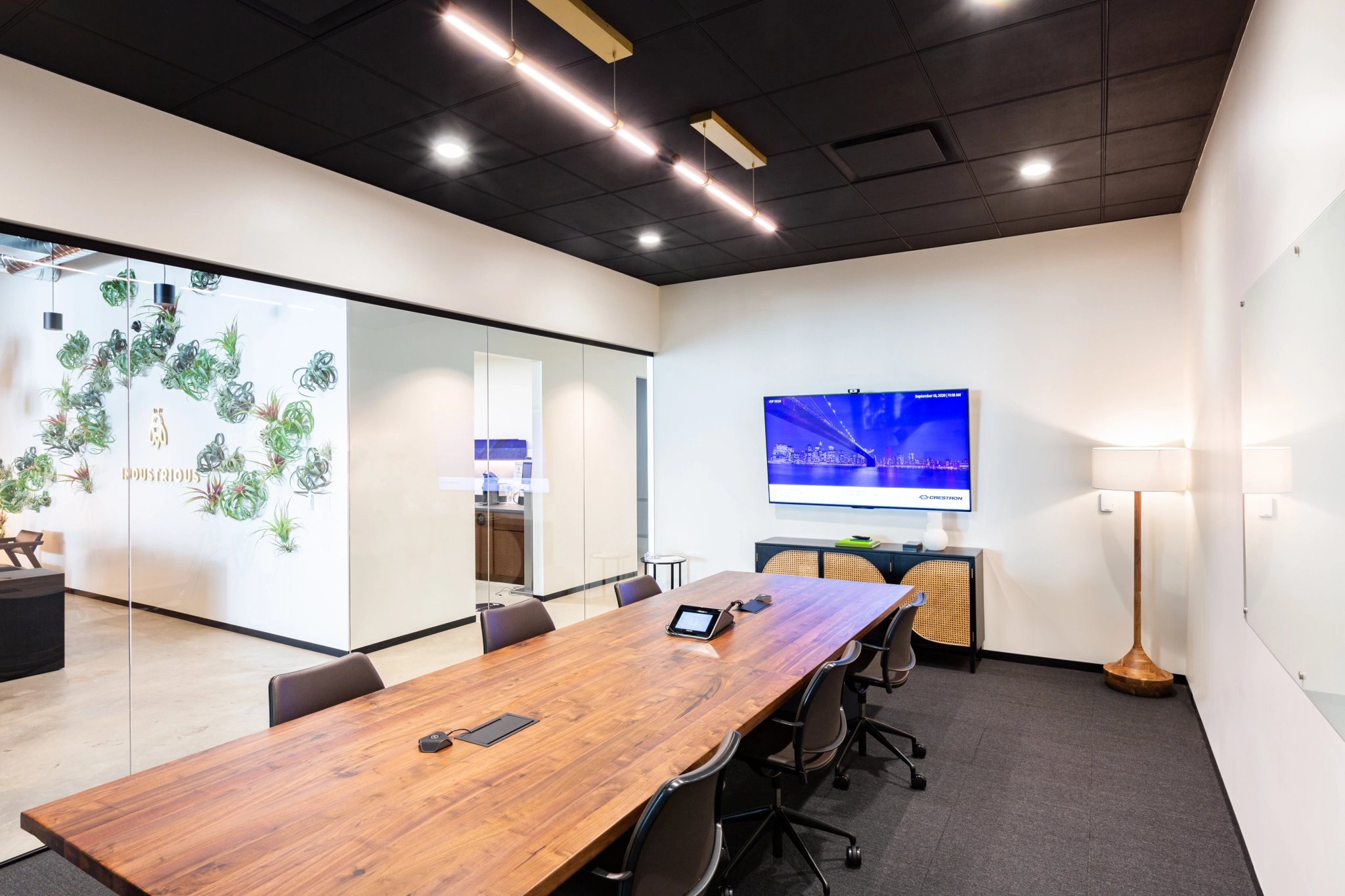 Modern meeting room with a long wooden table, several chairs, a large LED screen on the wall, and a glass partition separating the room from an adjacent office space in Walnut Creek, complete with plants and additional seating.