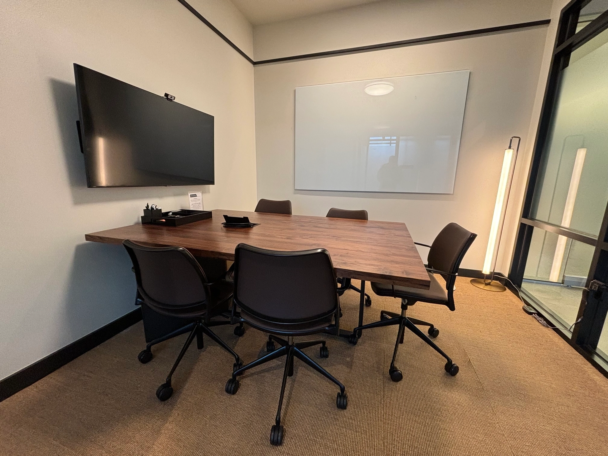 An office workspace with a conference room equipped with a table, chairs, and a TV.