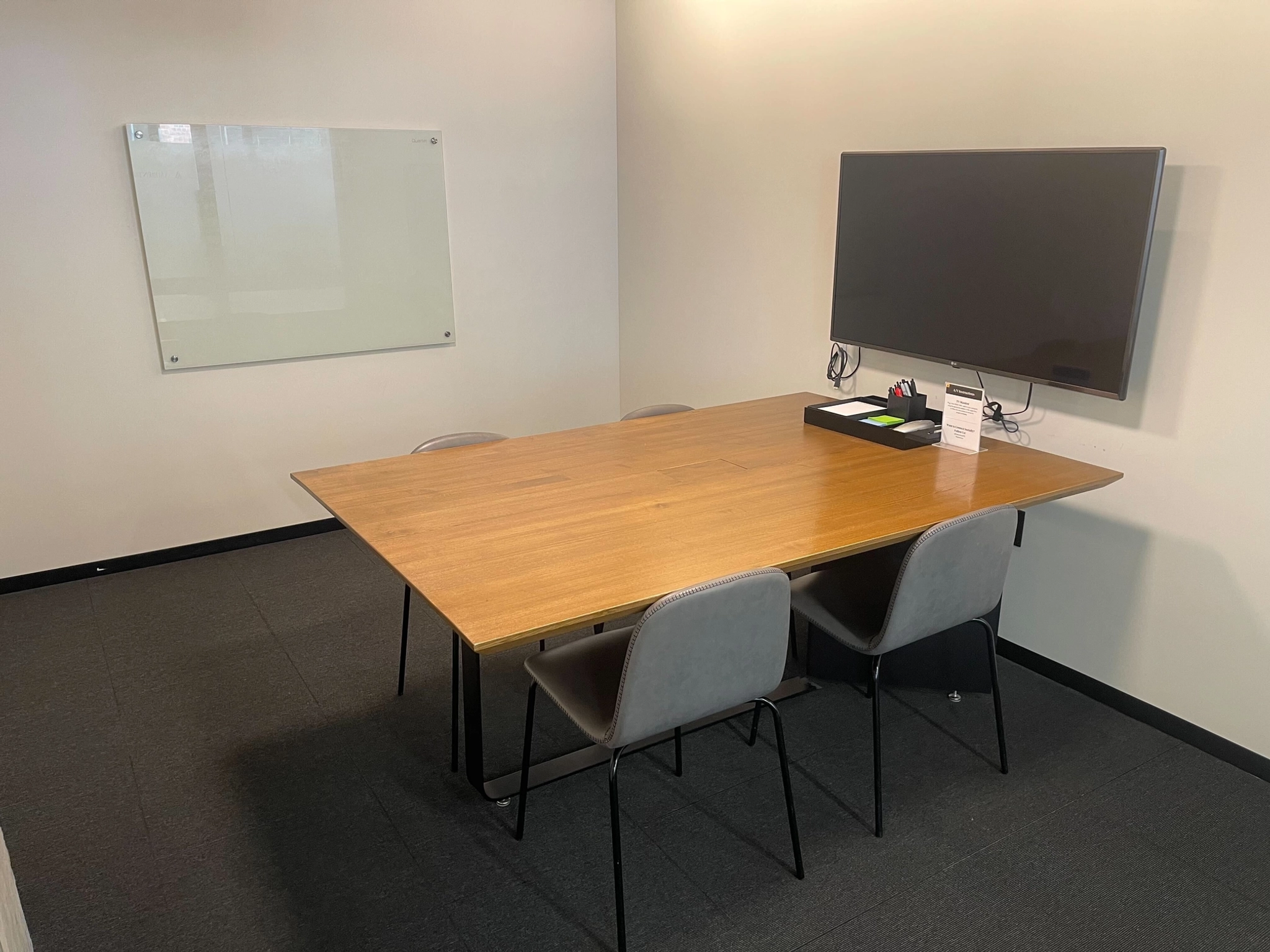 Une salle de réunion confortable dans l'espace de coworking comprend une table en bois, quatre chaises, une télévision murale et un tableau blanc.