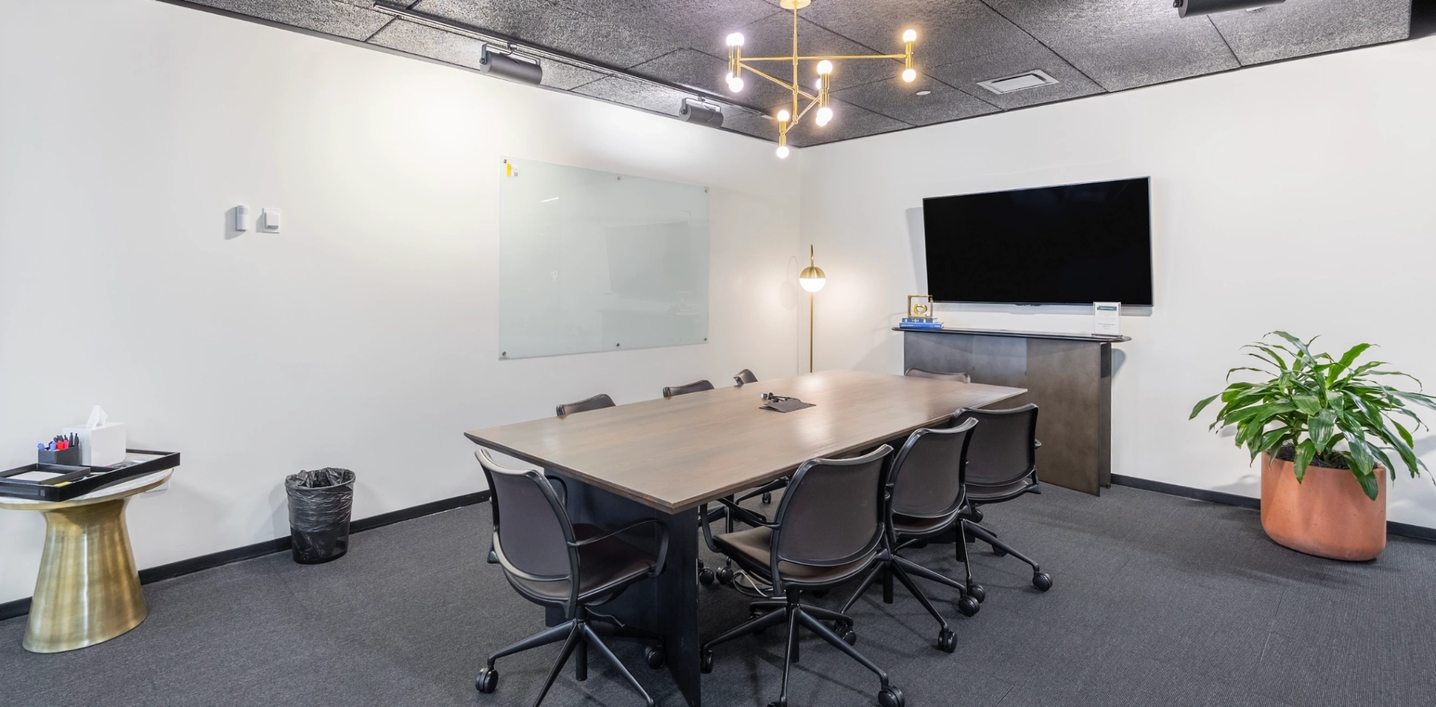 Een moderne coworking-conferentieruimte in Arlington, met een grote tafel, zes stoelen, een whiteboard, een aan de muur gemonteerde tv en een potplant.