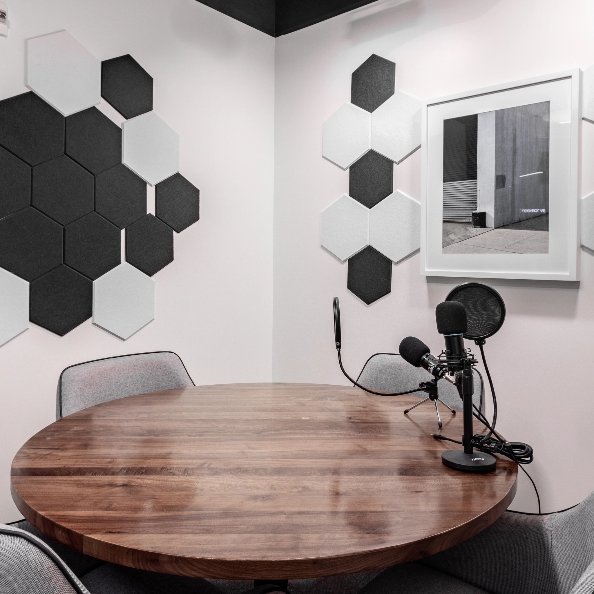 Un petit studio d'enregistrement de podcast à McLean avec une table ronde en bois, deux microphones sur pieds et des panneaux insonorisés hexagonaux sur les murs. Parfait pour les sessions de coworking, il comprend également une photo encadrée accrochée sur un mur, ajoutant une touche personnelle à cet espace de bureau confortable.