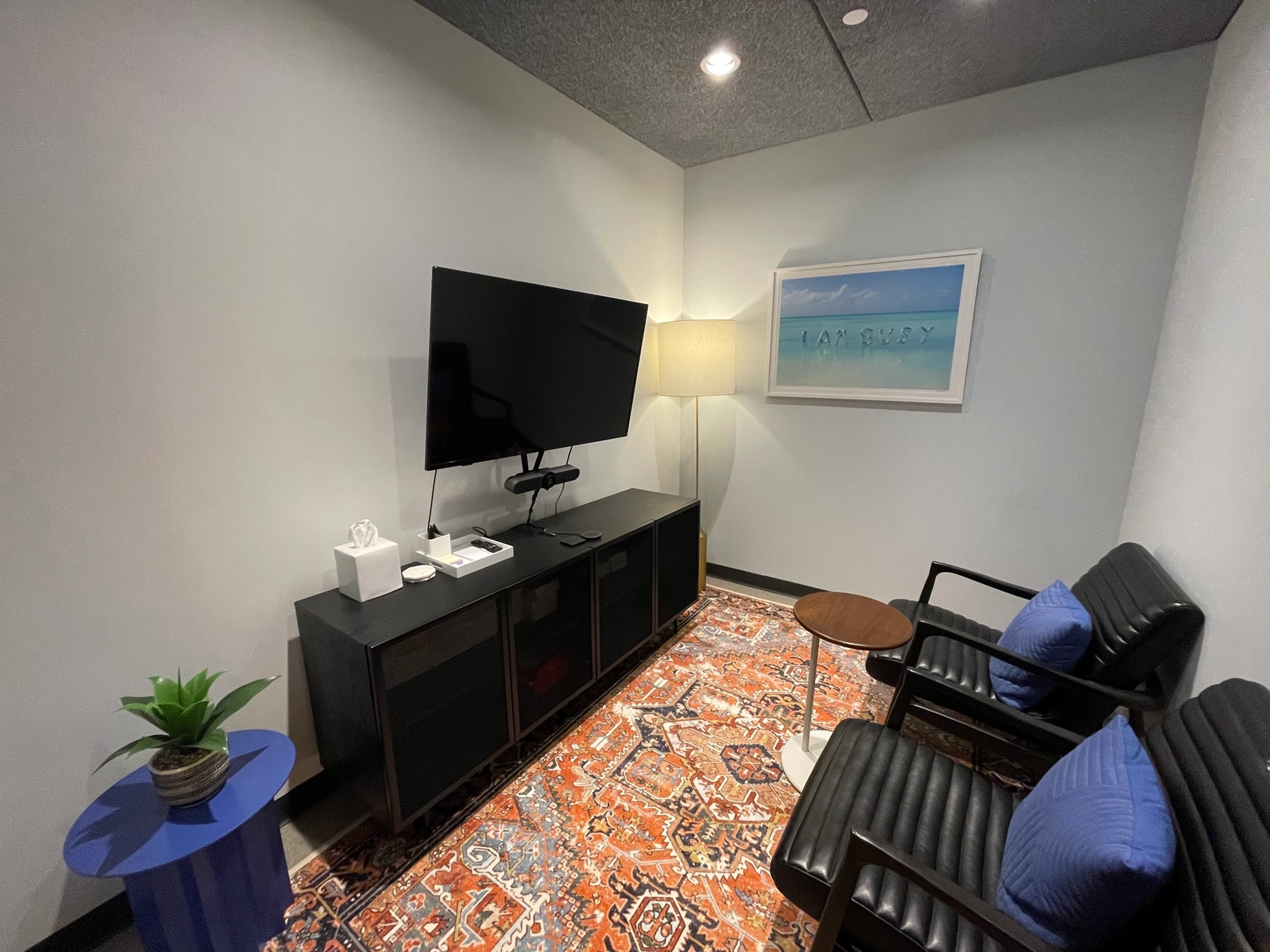 A meeting room with a tv, chairs and a rug.