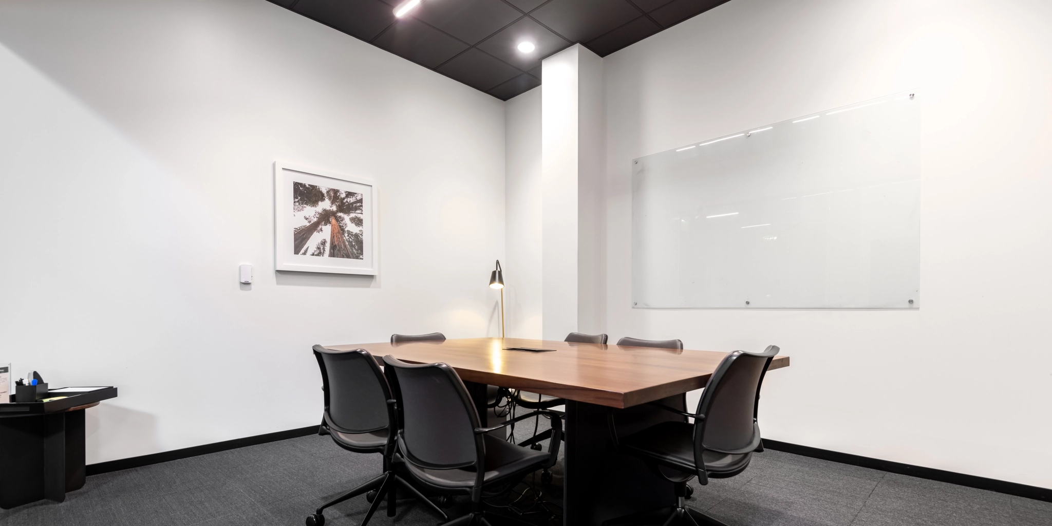 Une salle de réunion confortable à Walnut Creek comprend une table en bois, cinq chaises, des œuvres d'art murales, une lampe de bureau et un tableau blanc, parfaits pour vos besoins de coworking.