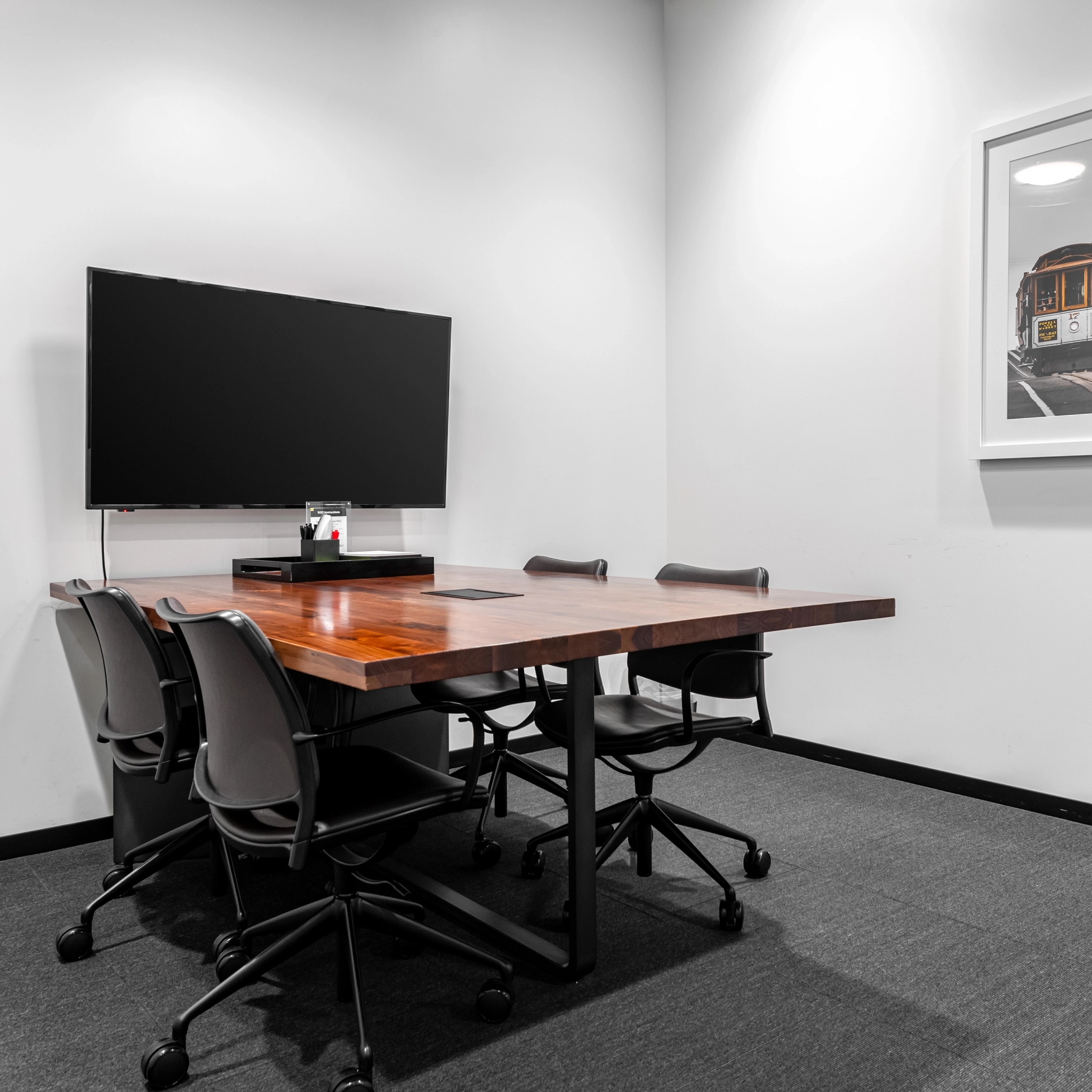 Une salle de conférence de coworking élégante dotée d'une table en bois, de quatre chaises, d'une télévision murale et d'œuvres d'art encadrées offre aux professionnels de Walnut Creek un espace de travail inspirant.