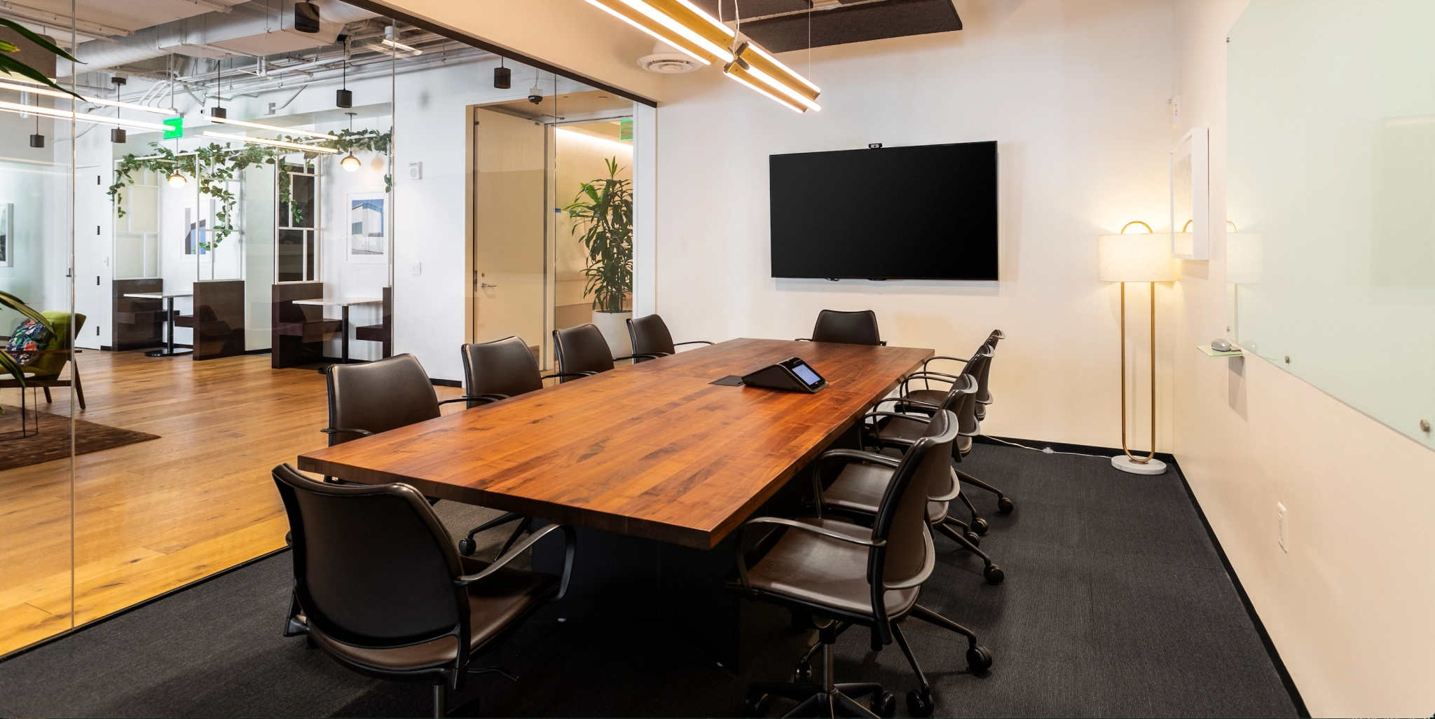 Een moderne vergaderruimte in ons kantoor in San Francisco beschikt over een lange houten tafel, zwarte stoelen, een grote aan de muur gemonteerde monitor en een whiteboard. De kamer heeft glazen wanden, waardoor er uitzicht is op aangrenzende ruimtes.