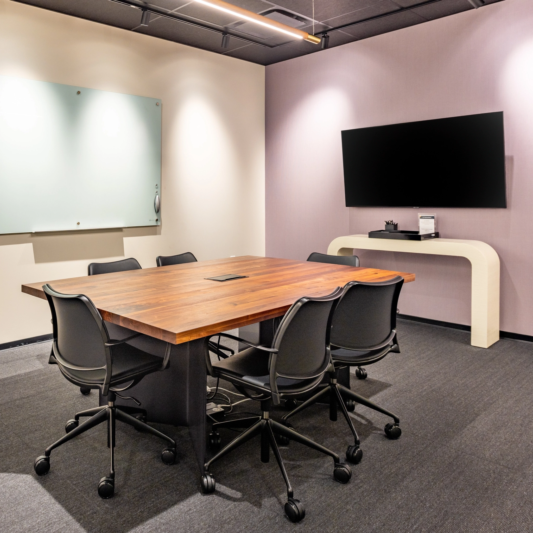 Een coworking-vergaderruimte in Washington, met een houten tafel, zes bureaustoelen, een aan de muur gemonteerd whiteboard en een aan de muur gemonteerde flatscreen-tv met een console eronder.