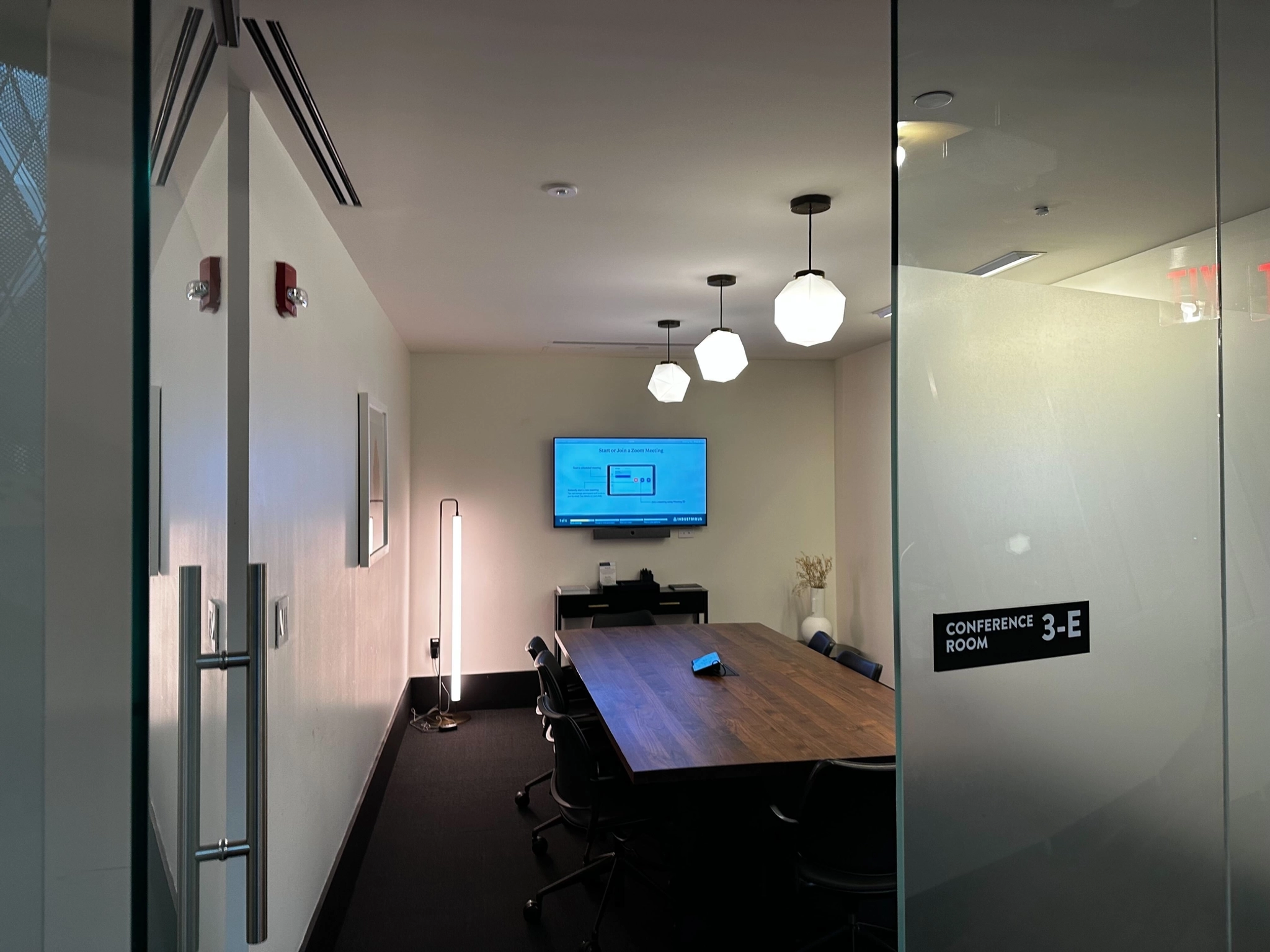 A modern conference room in a New York coworking space with glass doors and a tv.