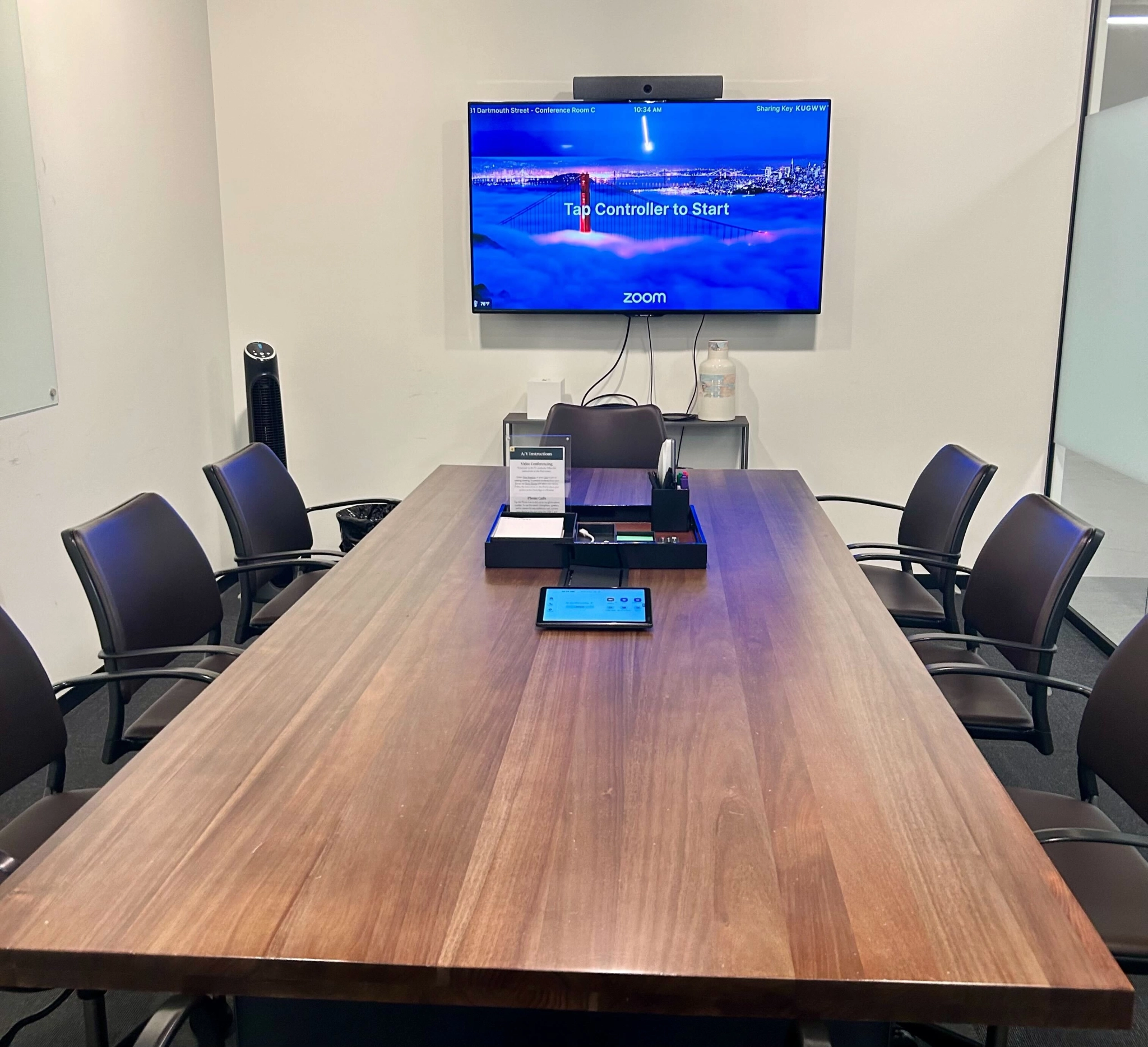 Een moderne coworking-conferentieruimte uitgerust met een groot scherm met een videoconferentie-interface, een lange tafel en verschillende stoelen.