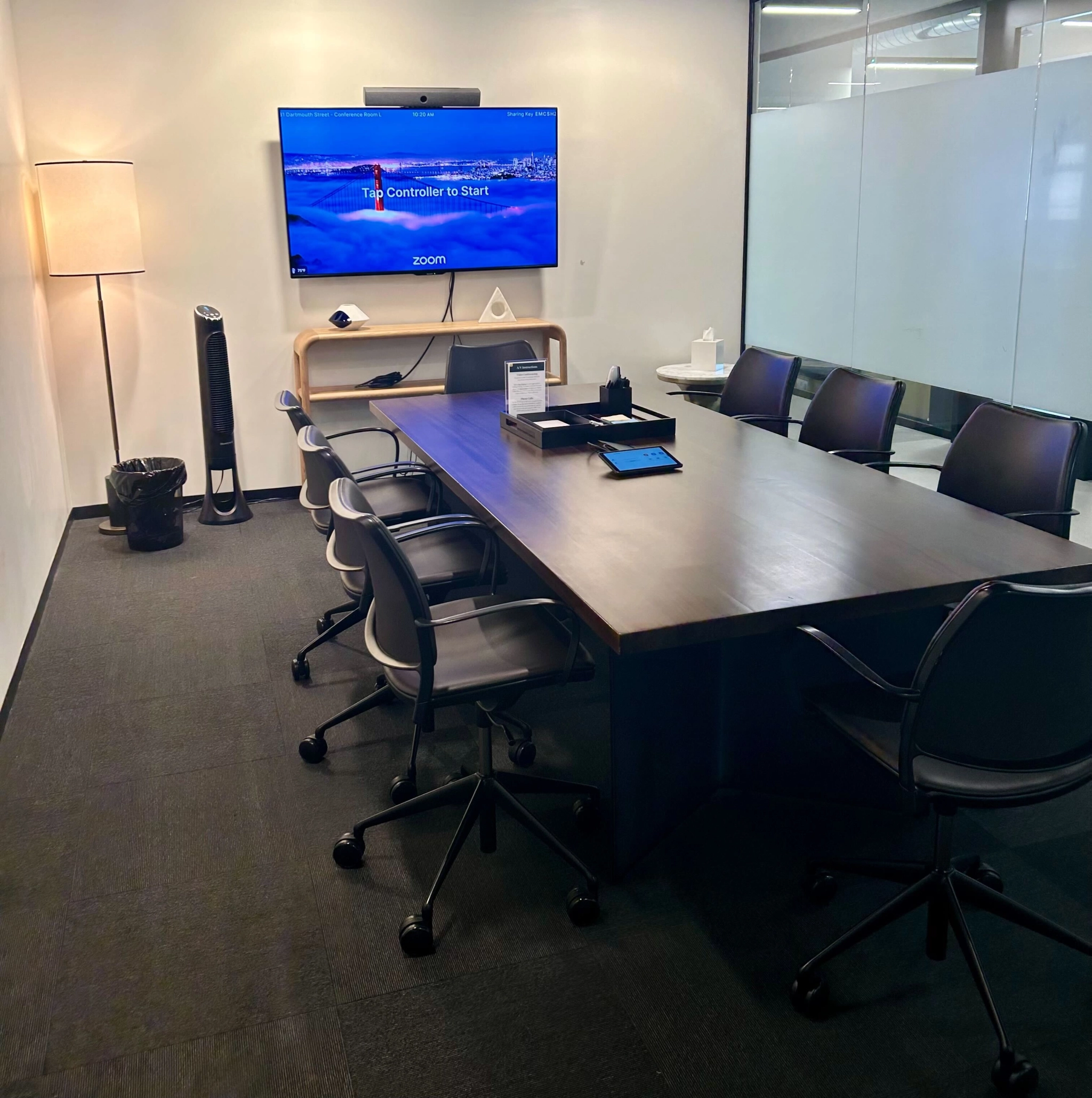 A modern meeting room with a large table, office chairs, and a television display showing a video call interface.