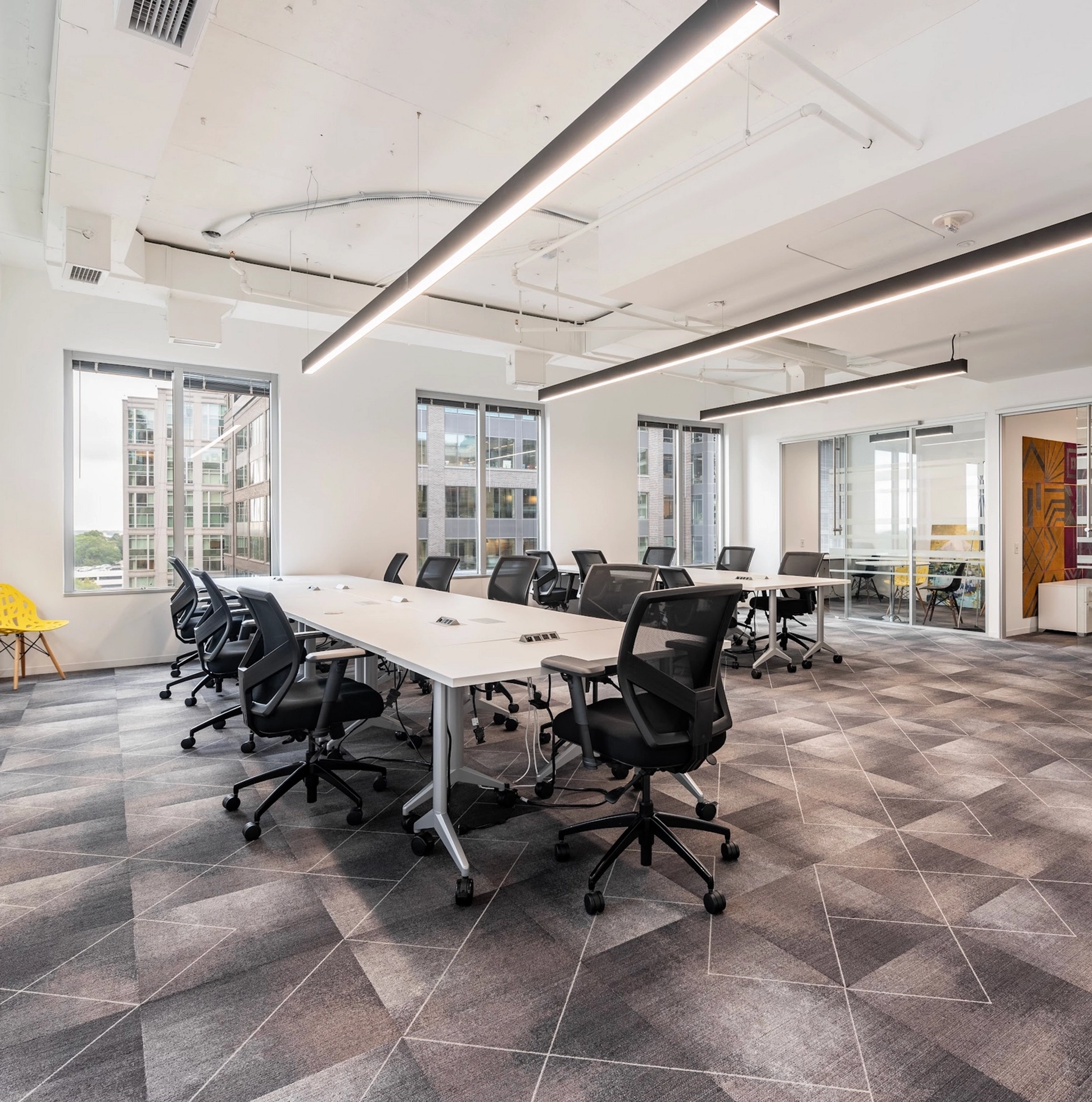 Espace de bureau moderne à Arlington avec de grandes fenêtres, une moquette à motifs géométriques, plusieurs chaises noires à roulettes et des bureaux blancs. L'espace de travail bien éclairé bénéficie d'un éclairage fluorescent au plafond.