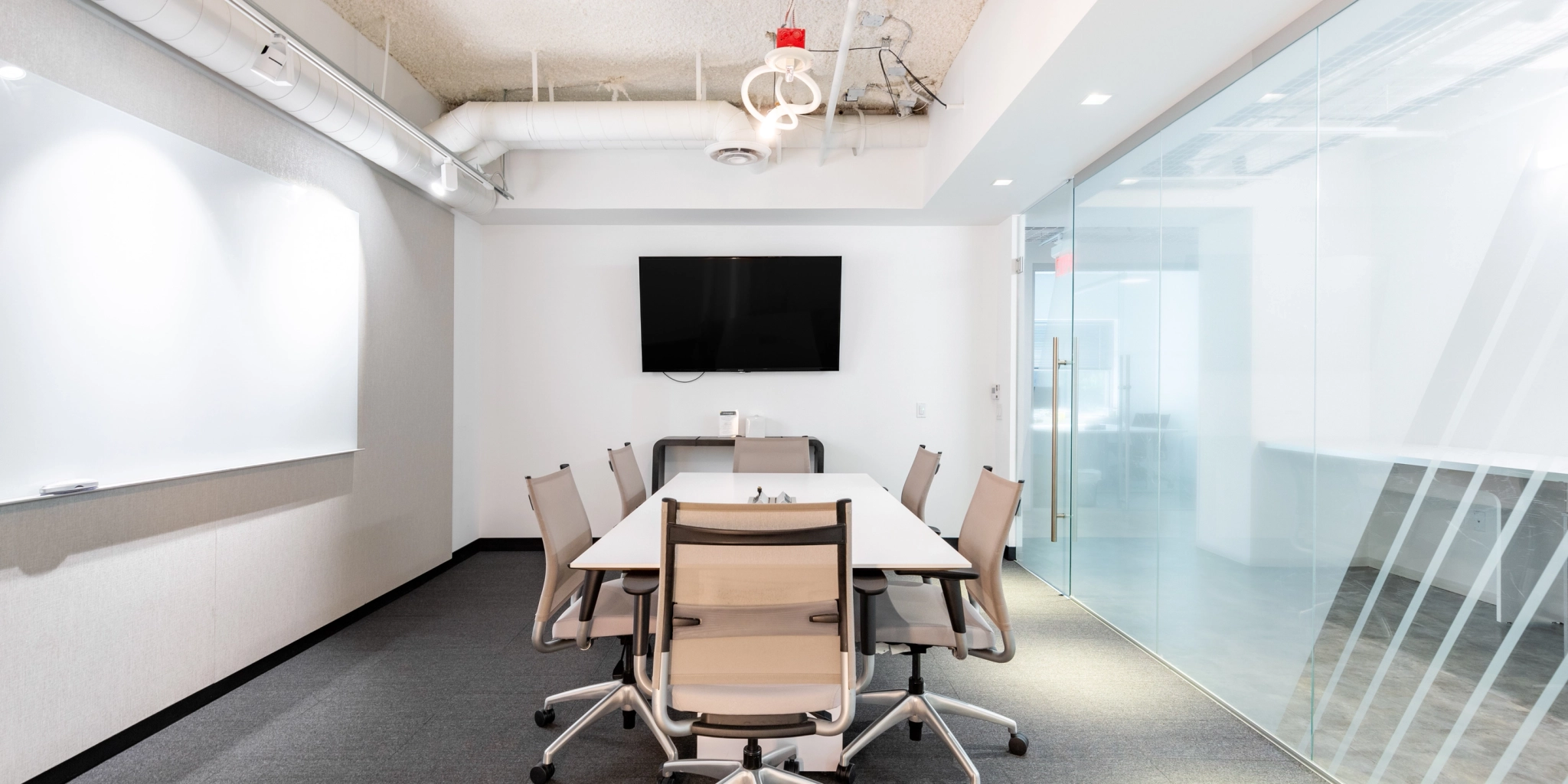 A modern coworking space in Arlington featuring a conference room with a table, six chairs, a wall-mounted screen, whiteboard, and glass wall.