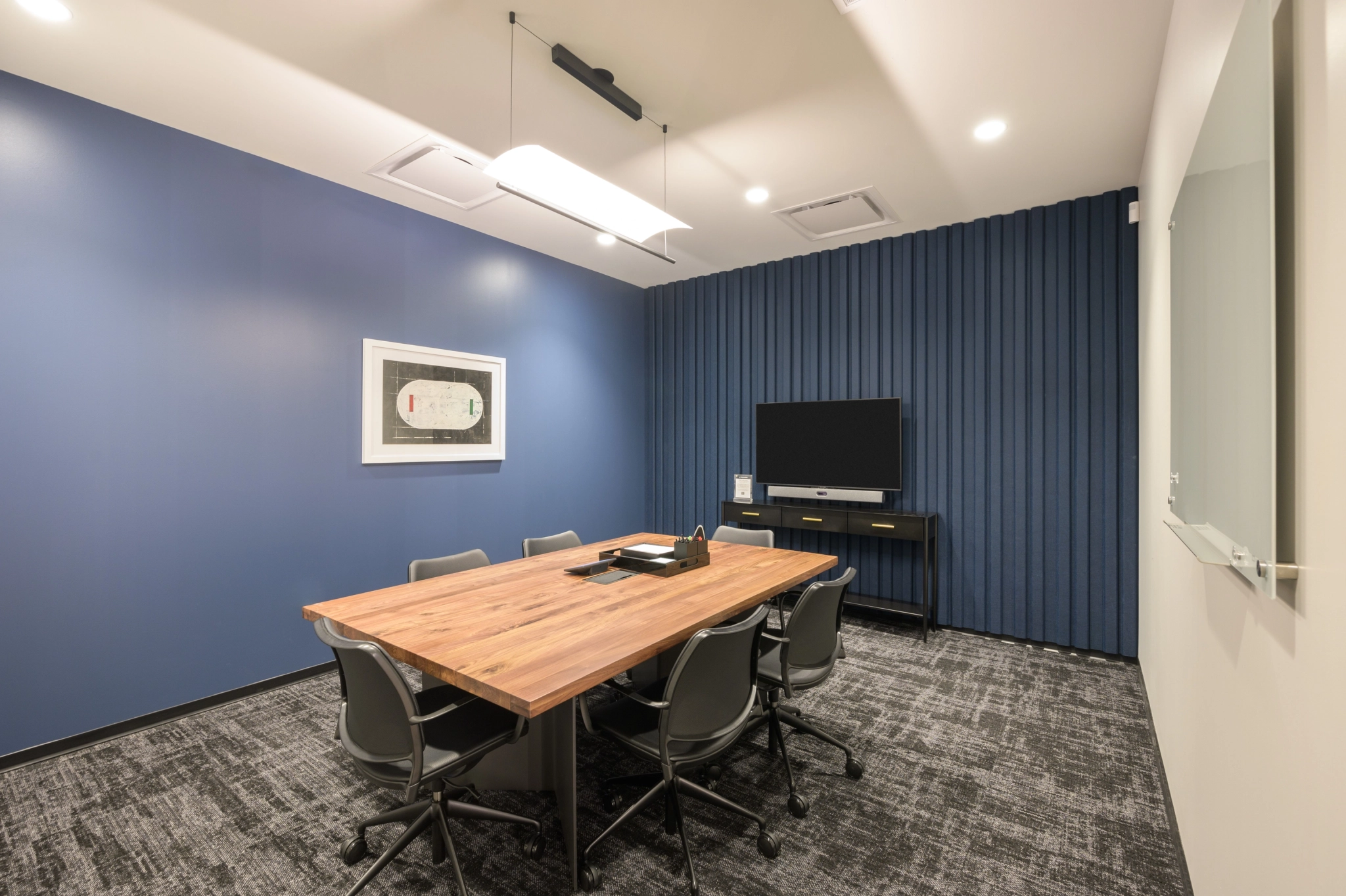 Salle de réunion de bureau de coworking moderne avec des murs bleus, une table de conférence en bois et une télévision au mur.