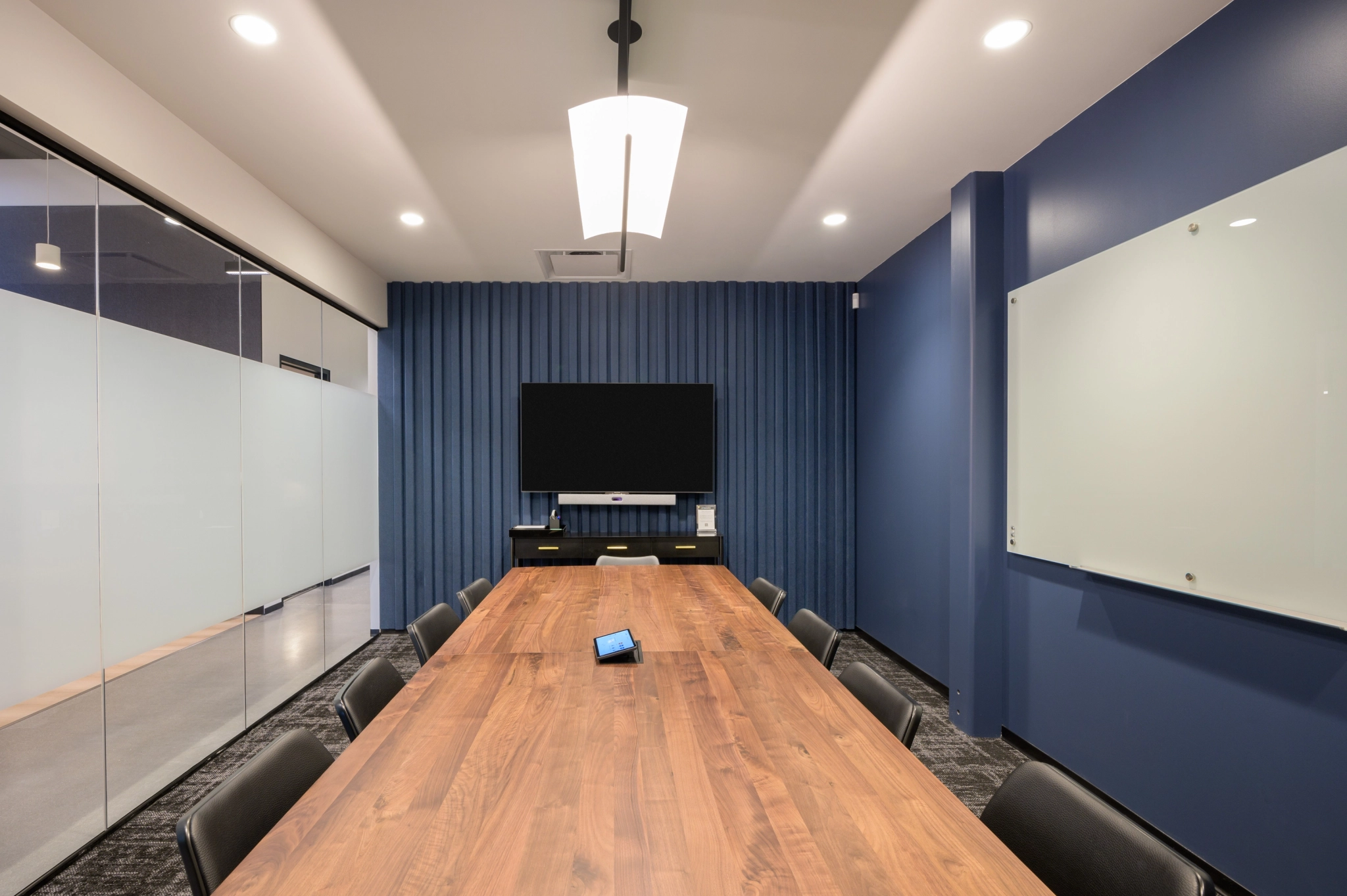 Modern coworking space in Denver featuring a long wooden table, black chairs, a large screen on the wall, and glass partitions.