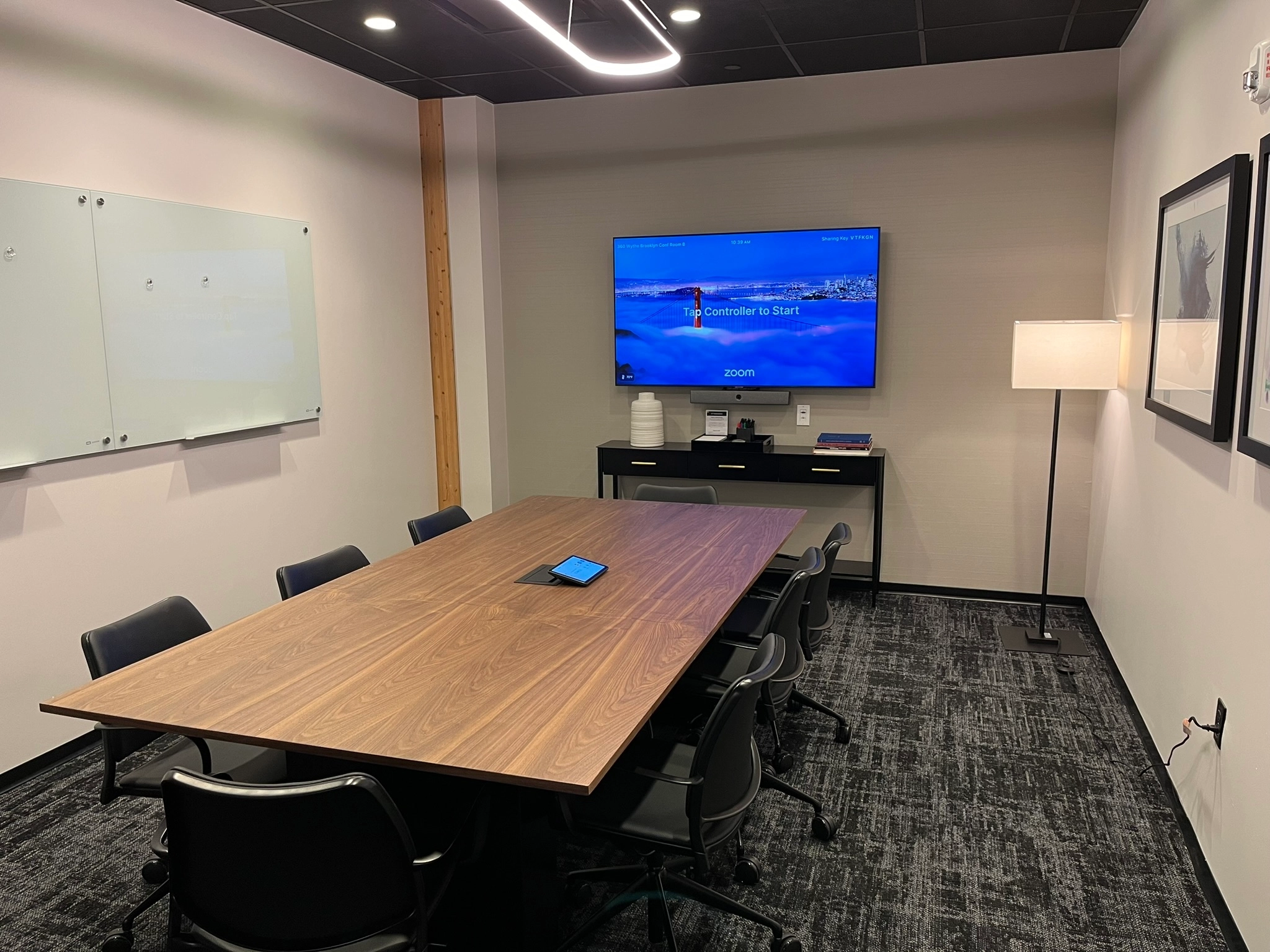 A modern coworking conference room in Brooklyn with a large table, chairs, and a television display prepared for a video call.