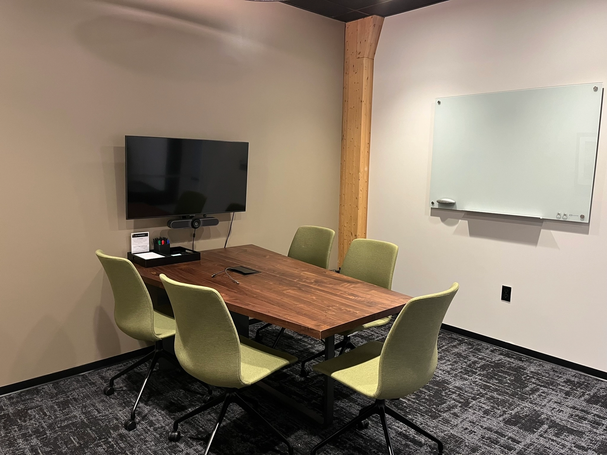 Salle de réunion moderne avec table en bois, chaises vertes, télévision et tableau blanc.