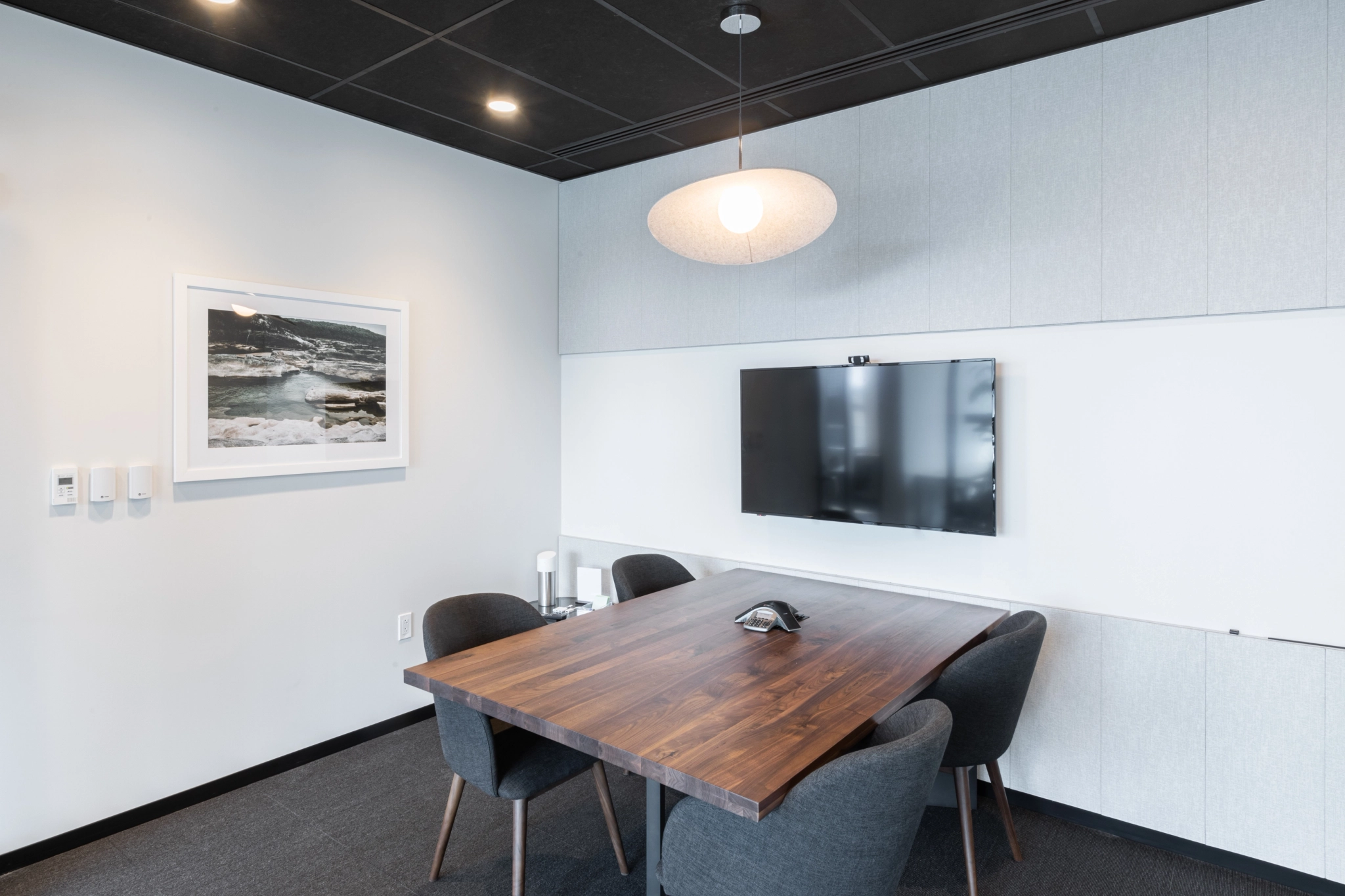 Une salle de conférence de bureau moderne à North Bethesda avec une table en bois, des chaises grises, une télévision murale et des œuvres d'art encadrées au mur.