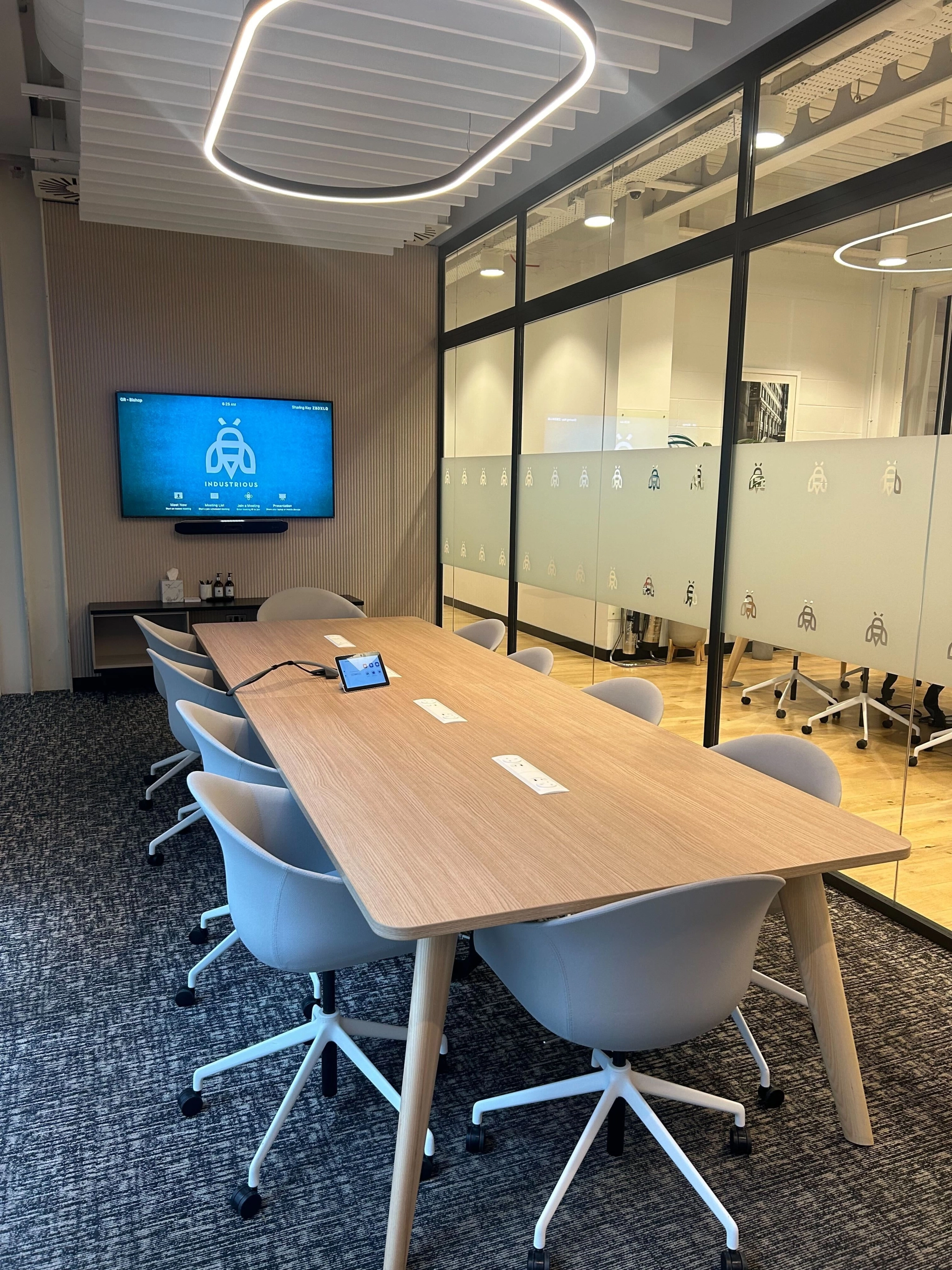 A modern conference room in a vibrant London coworking space features a long wooden table, white chairs, a wall-mounted screen, and frosted glass partition.