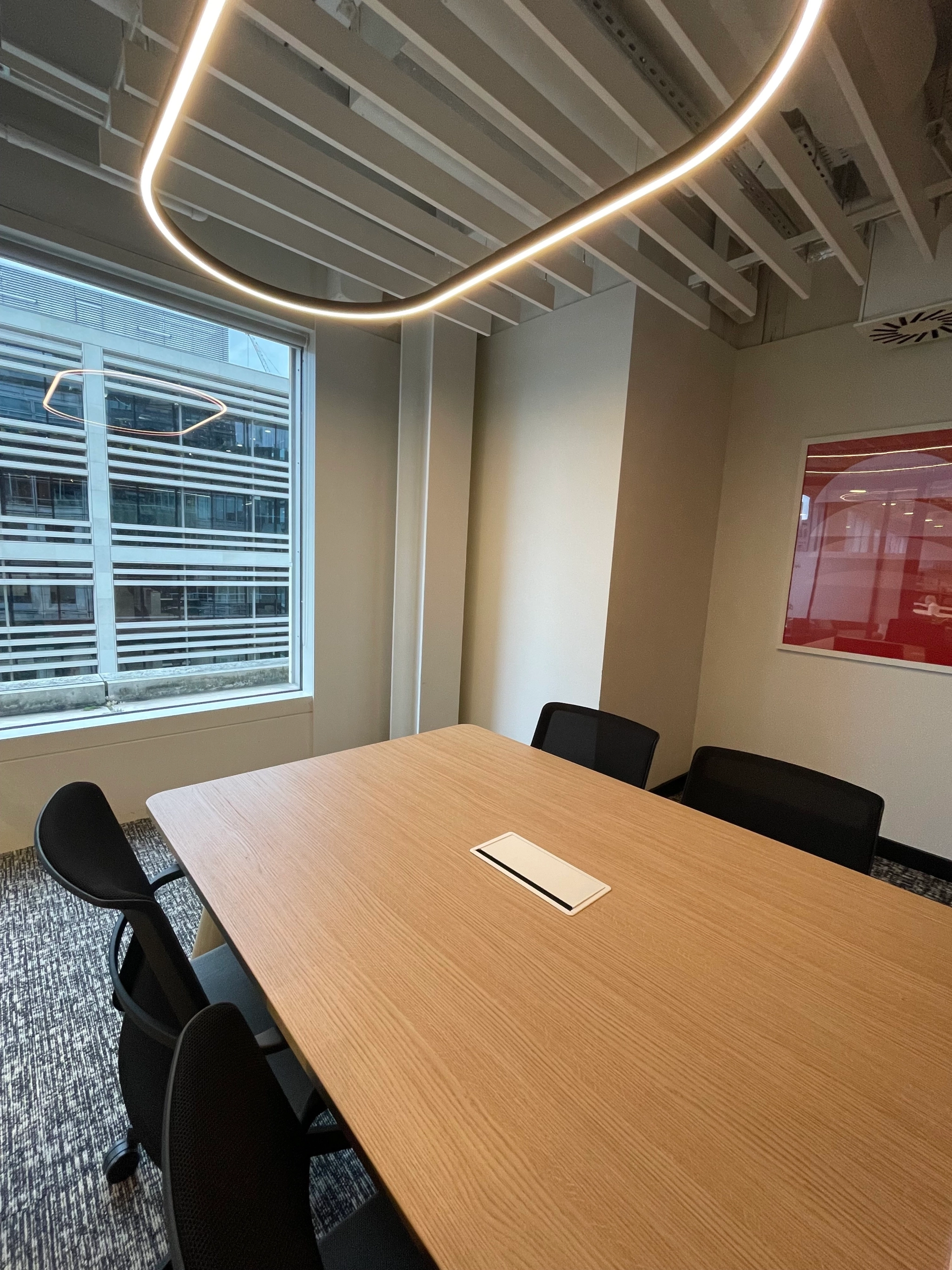 A small meeting room in London featuring a wooden table, five black chairs, a window, and modern ceiling lights.