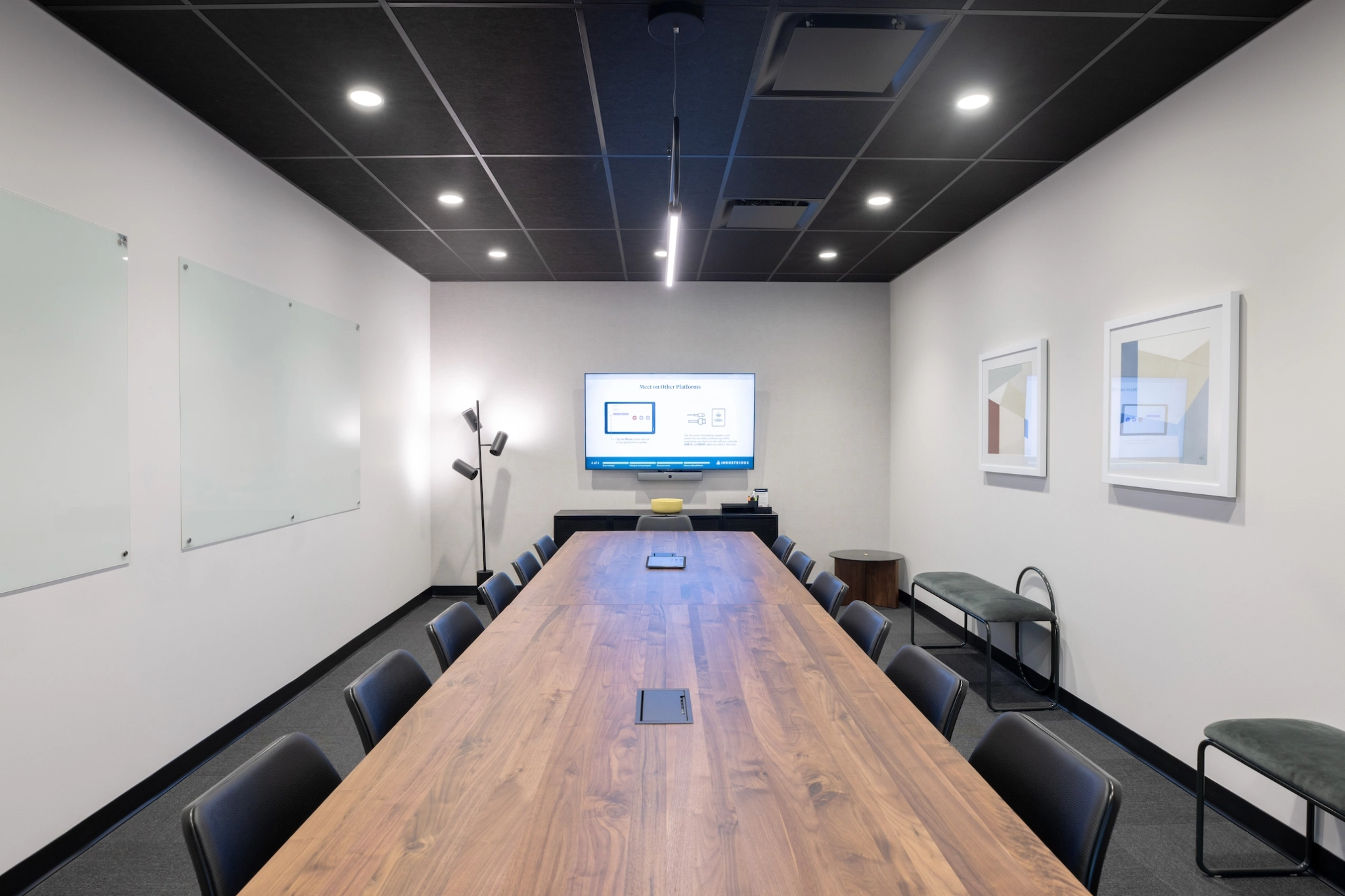 A modern conference room in a Houston office featuring a long wooden table, black chairs, a wall-mounted screen, whiteboards on the left wall, and framed artwork on the right wall.