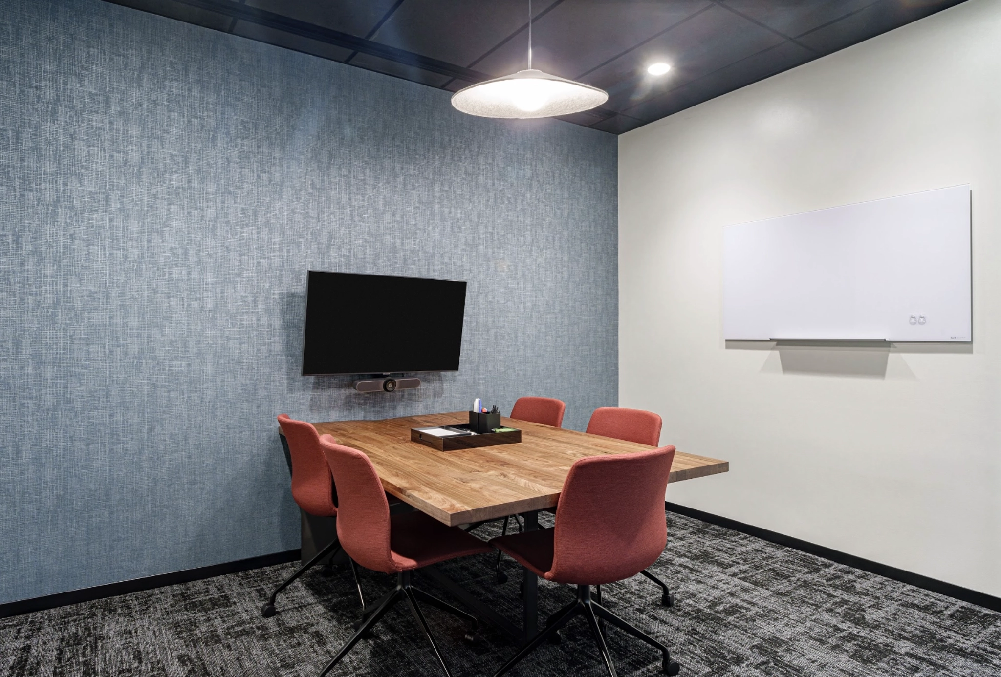 A small conference room in a coworking space features a wooden table, four red chairs, a wall-mounted TV, a whiteboard, and a ceiling light—perfect for productive meetings in the heart of Austin.