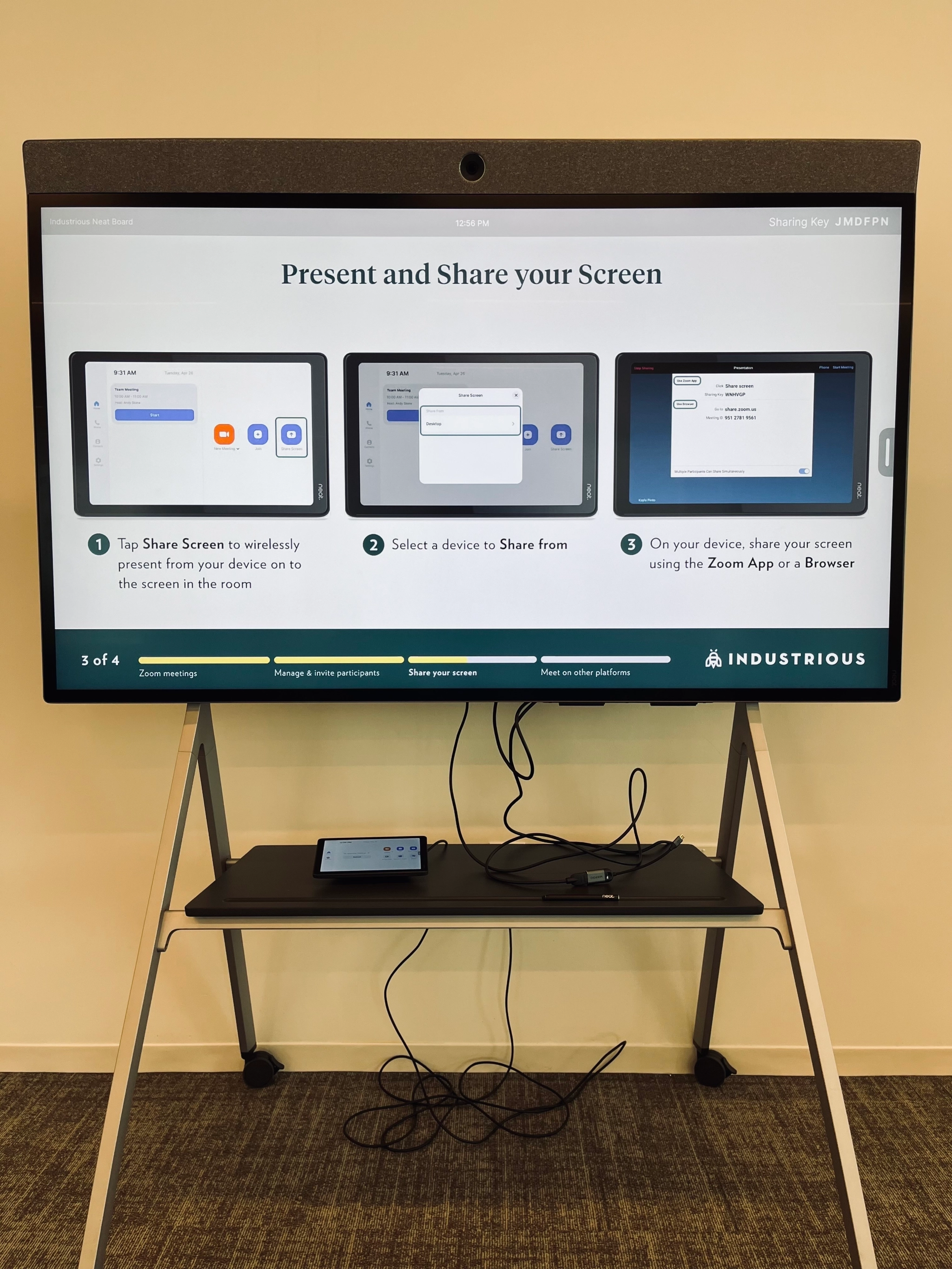 Instructional display showing steps to present and share a screen in your Austin workspace: connect your device, select a sharing option, and use the Zoom app or browser. In the meeting room, a tablet rests on a stand below the display.