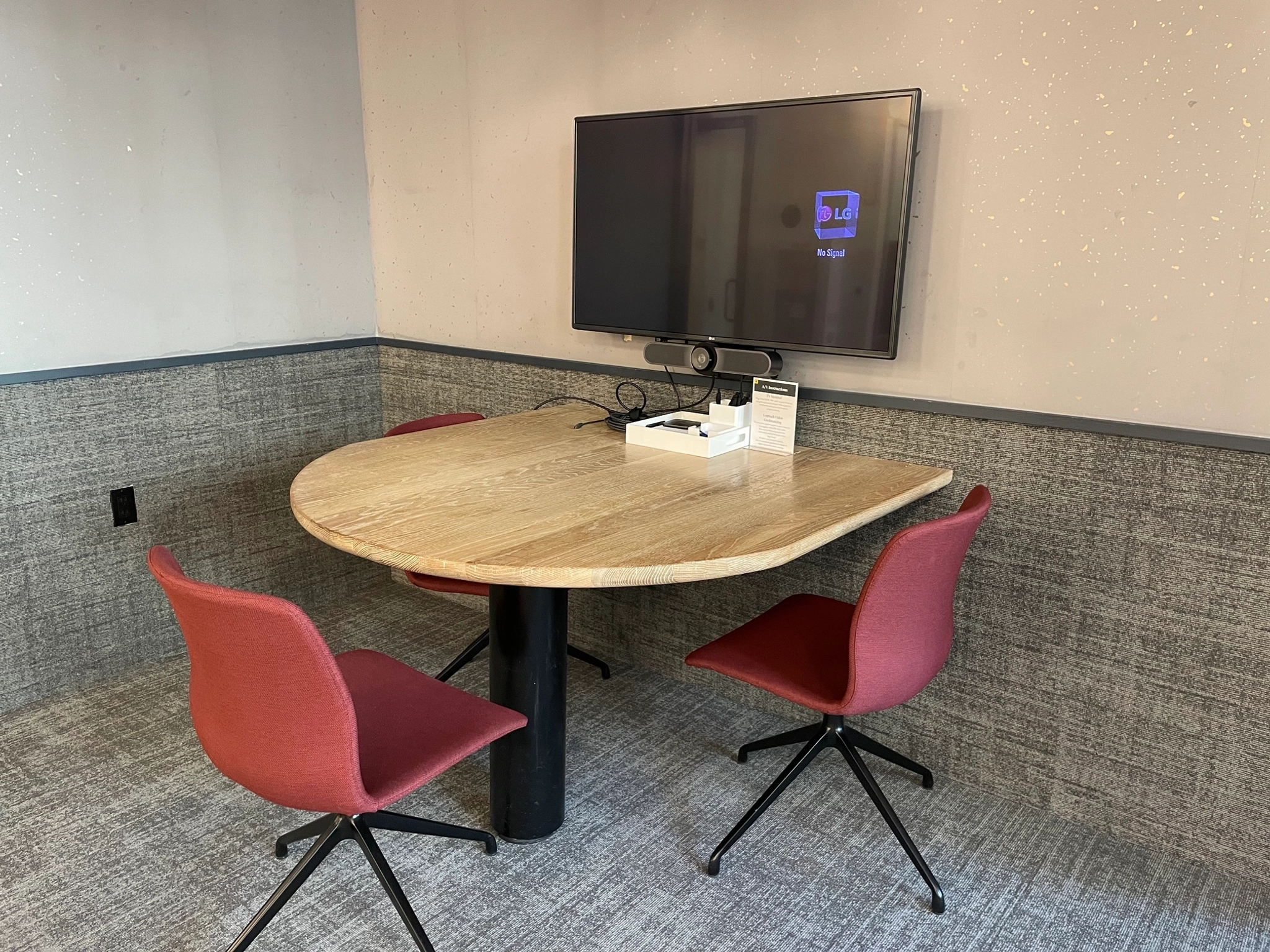 Cómoda sala de reuniones tipo office con mesa ovalada de madera, tres sillas de color rojo vivo y un biombo de pared, perfecta para tus reuniones de negocios en Nueva York.