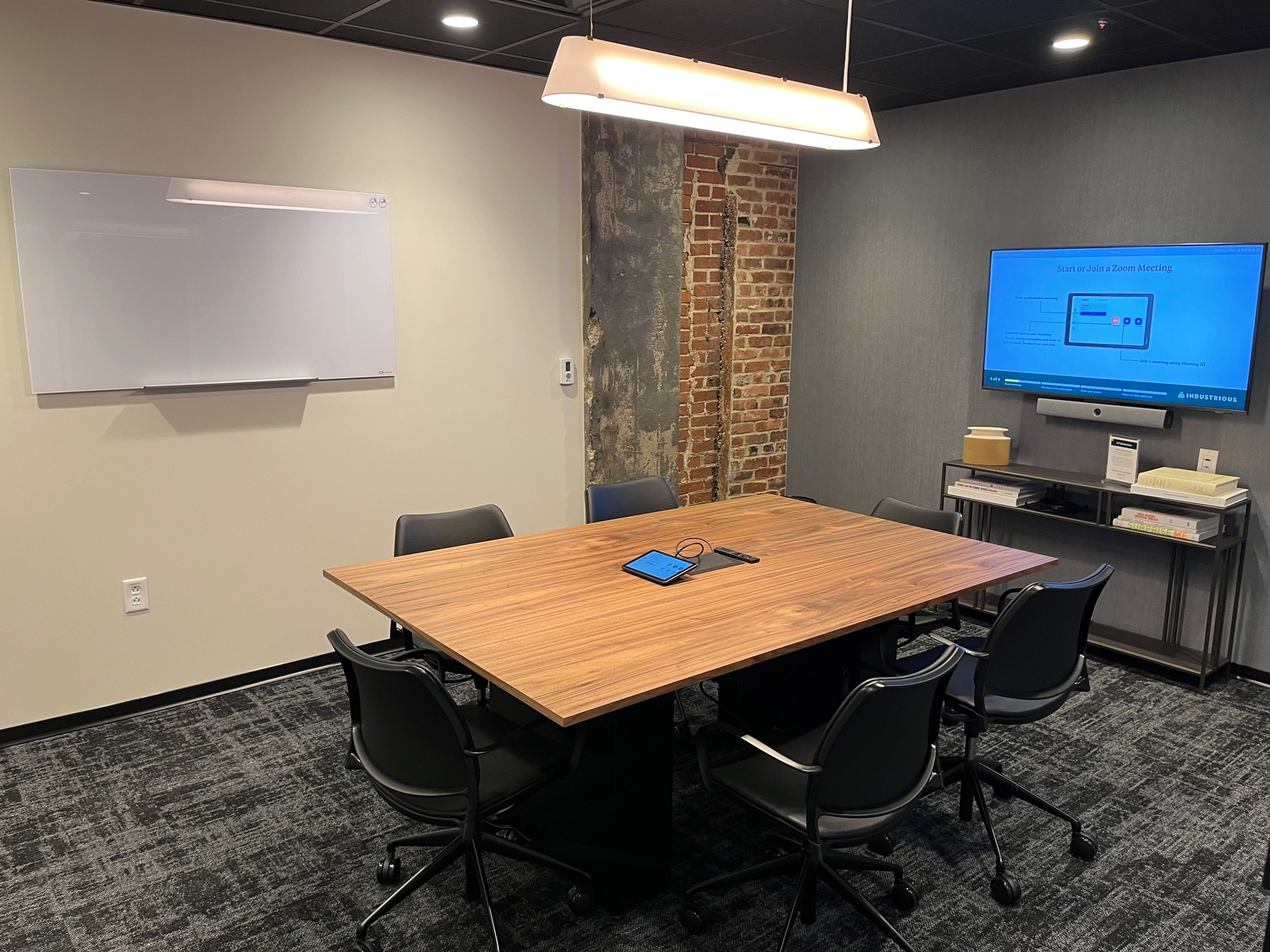 Een moderne coworking-conferentieruimte in Nashville beschikt over een houten tafel, zes stoelen, een aan de muur gemonteerd whiteboard en een scherm met een presentatie.