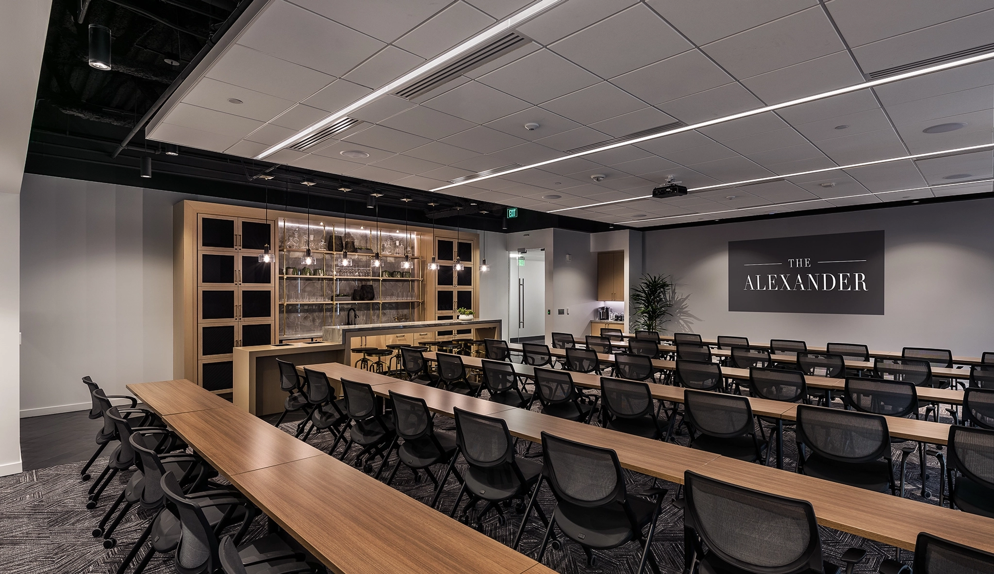 A modern meeting room with rows of tables and chairs, a wooden shelving unit, and a sign that reads "The Alexander" on the wall, perfect for any Chandler office setting.