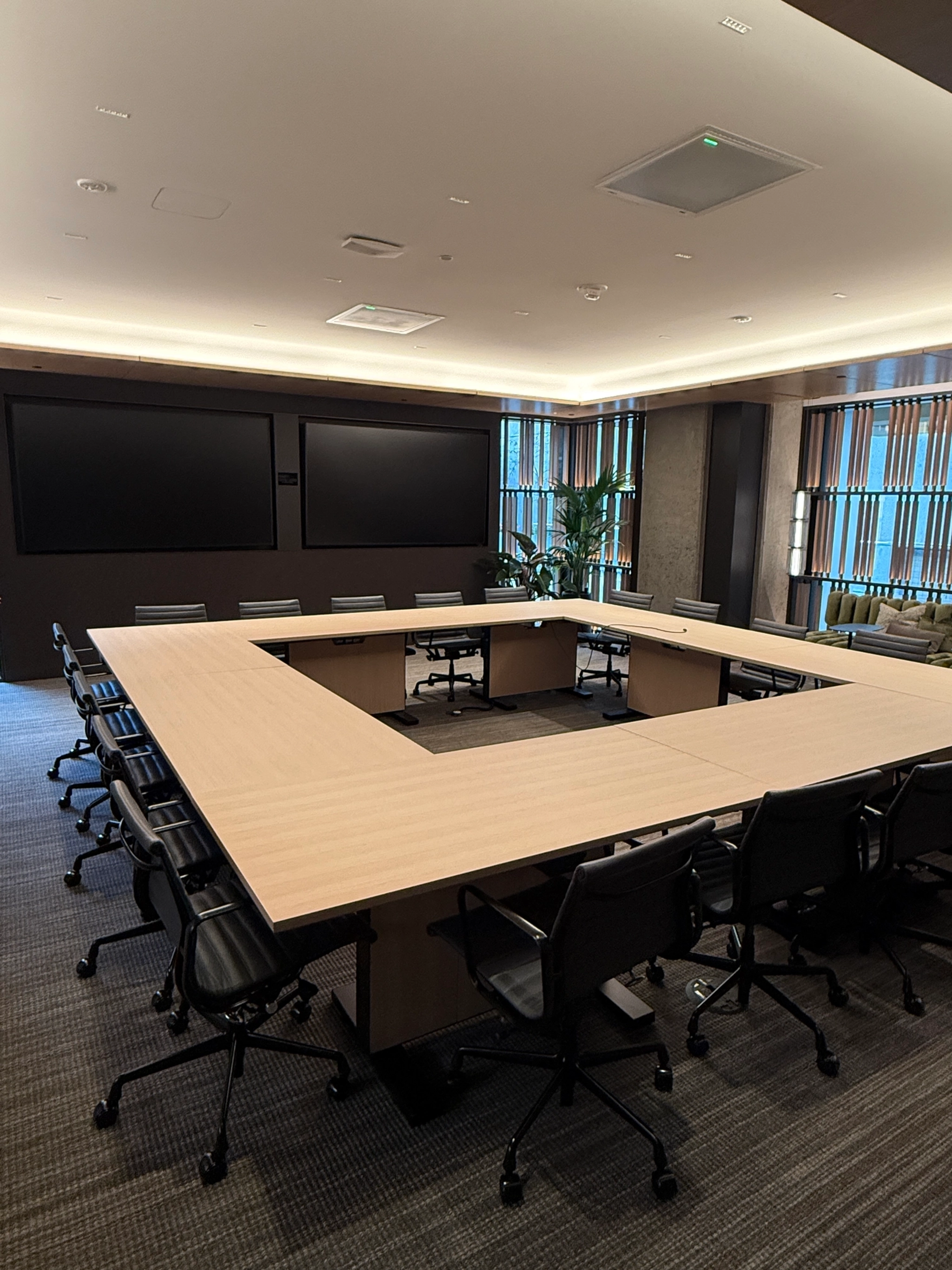 A modern coworking conference room with a rectangular table arrangement, surrounded by black chairs, embodies the dynamic spirit of San Francisco. Large windows draped with curtains illuminate this versatile workspace.