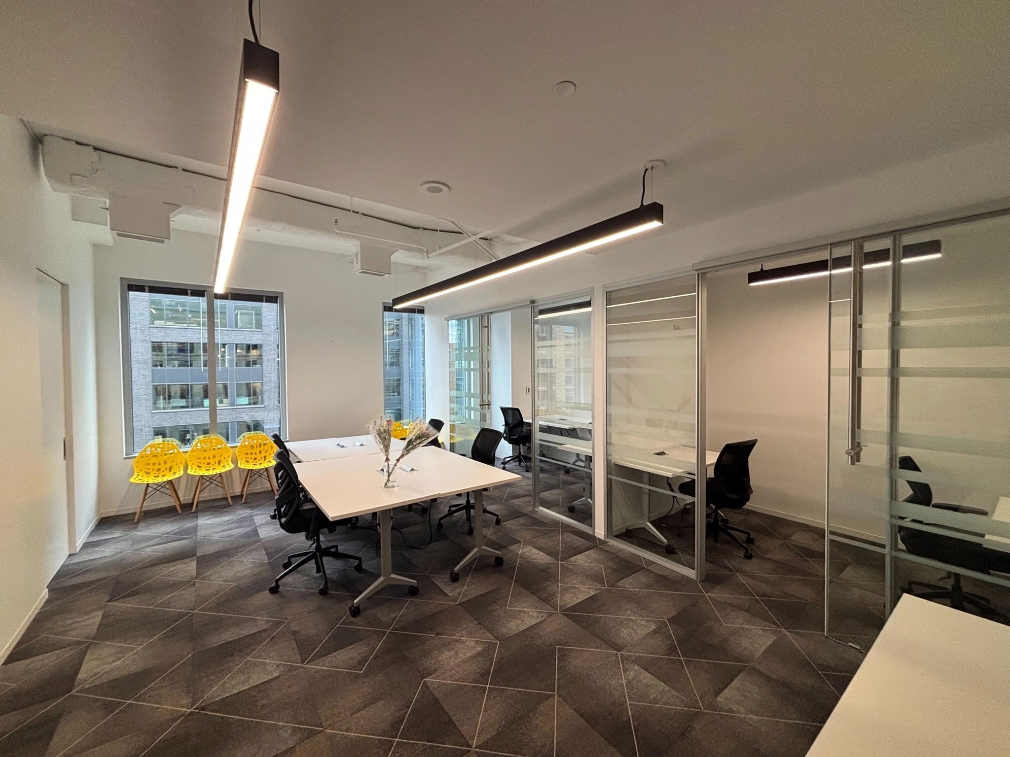 Modern Arlington office space featuring white desks, black office chairs, large windows, glass-walled meeting rooms, and a row of yellow chairs along one wall.