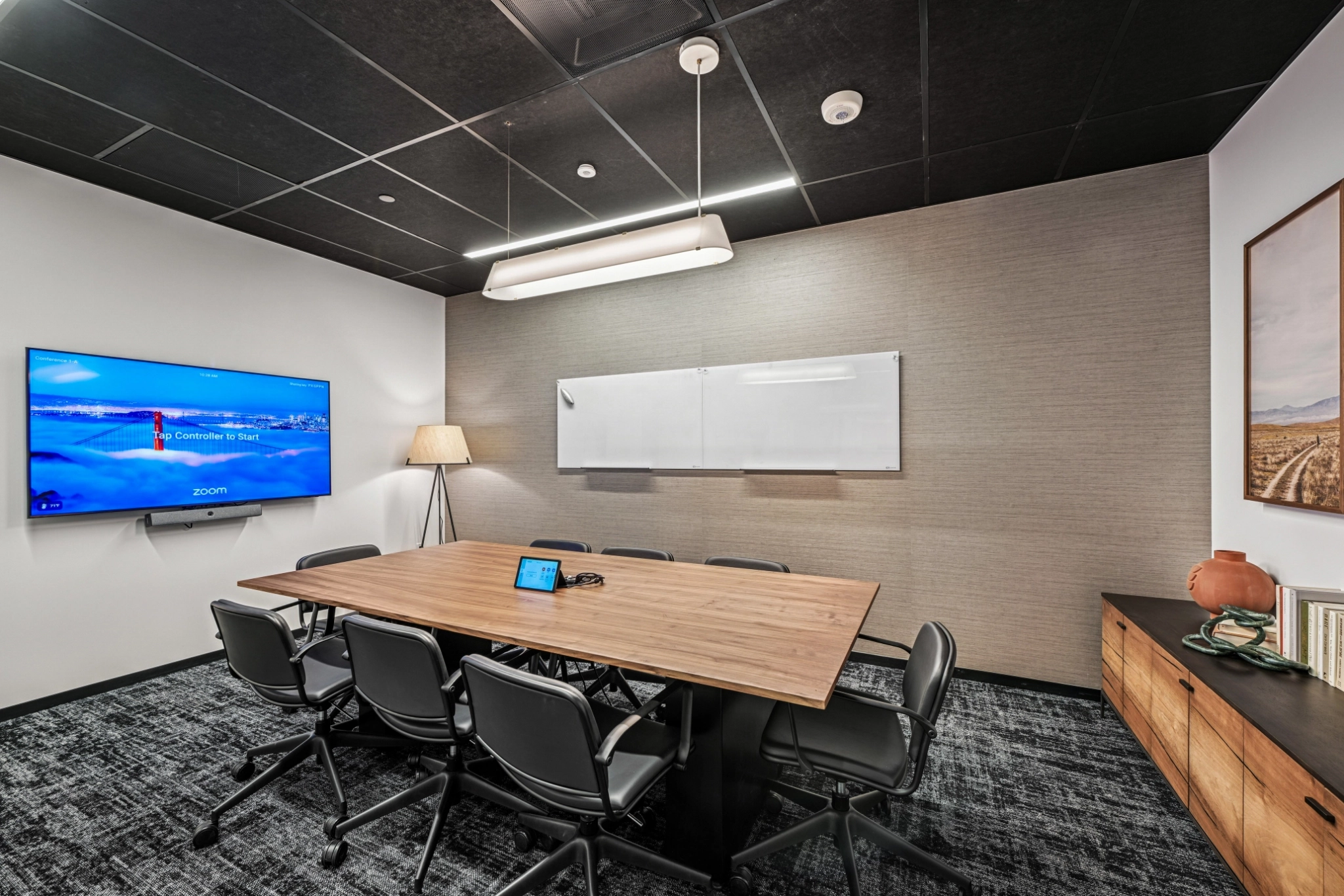 Modern office meeting room with a wooden table, six chairs, wall-mounted Zoom screen, whiteboard, floor lamp, and sideboard with decorative items—a stylish workspace designed for productivity.