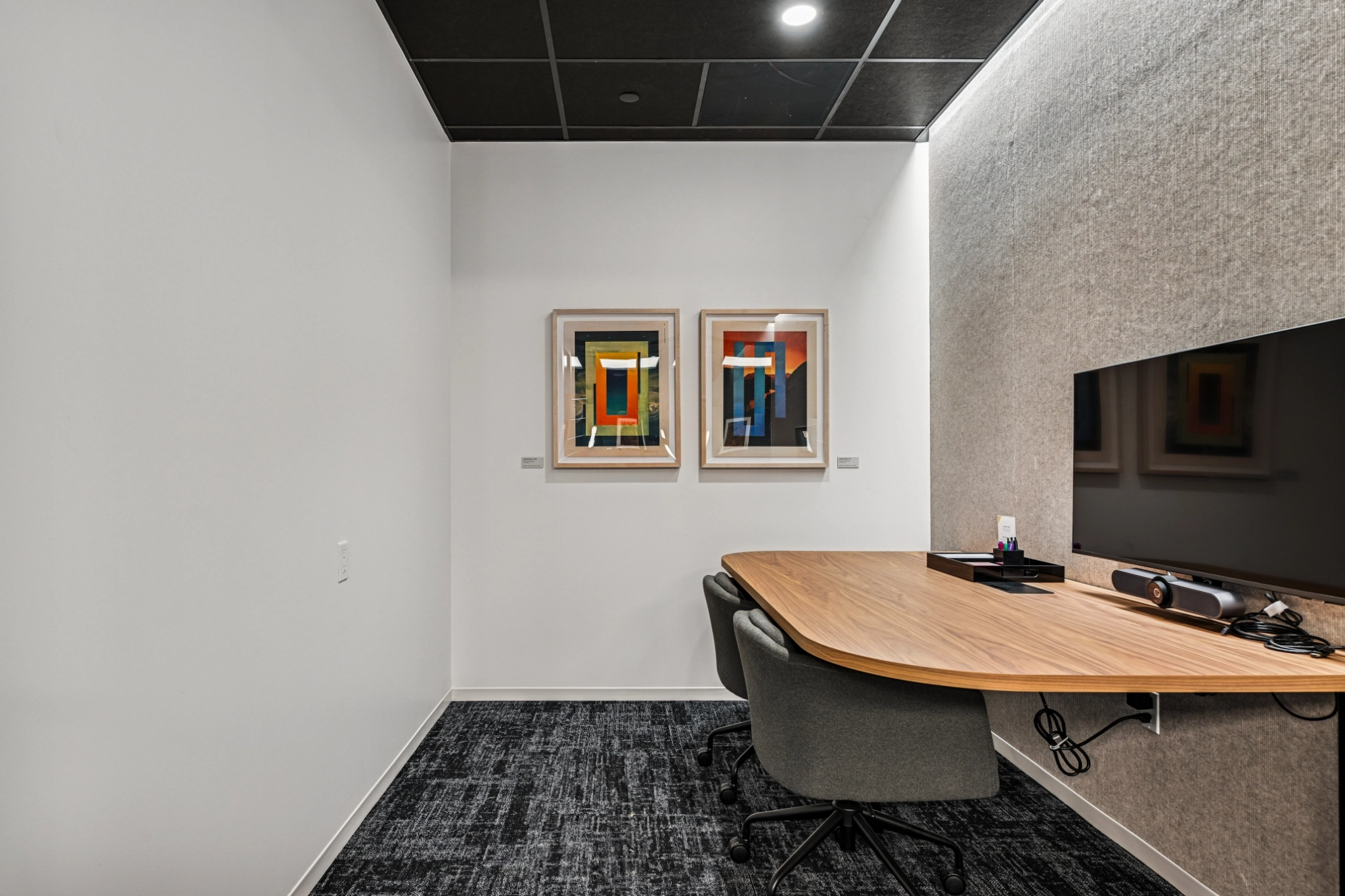 Sleek Beverly Hills workspace featuring a wooden desk, two gray chairs, a wall-mounted monitor, and two abstract art pieces on a crisp white wall.