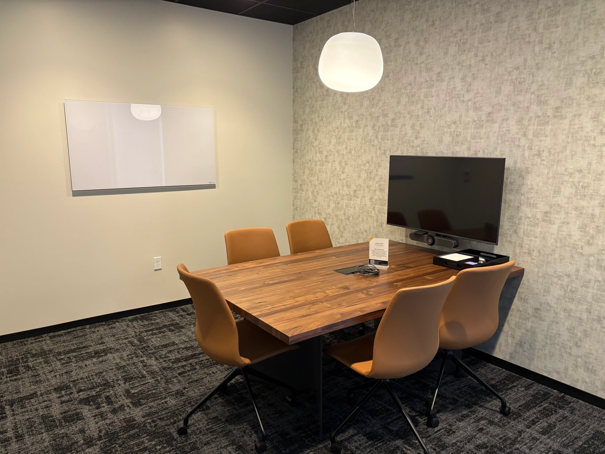 A small San Diego meeting room featuring a wooden table, five brown chairs, a wall-mounted TV, a whiteboard, and a pendant light—perfect for your next workspace session.