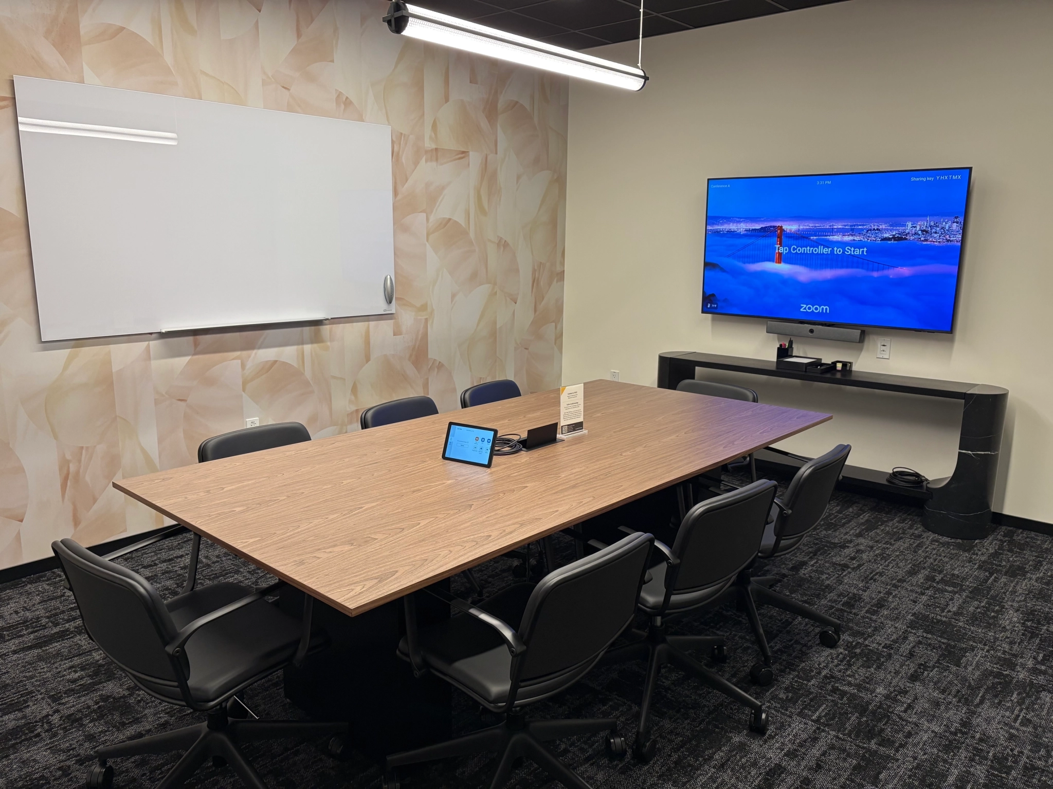 A modern East Palo Alto conference room with a long table, eight chairs, a wall-mounted TV displaying the Zoom app, a whiteboard, and a tablet on the table—perfect for coworking or team meetings.