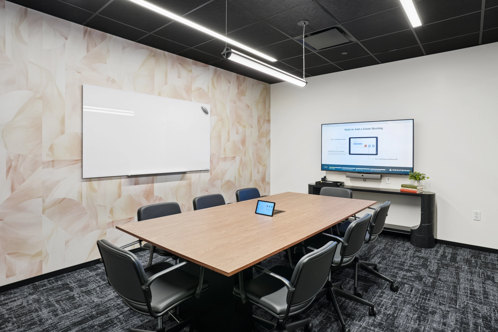 A modern meeting room in East Palo Alto featuring a rectangular table, eight chairs, a wall-mounted whiteboard, and a large screen displaying a Zoom interface—ideal for coworking and collaborative sessions.